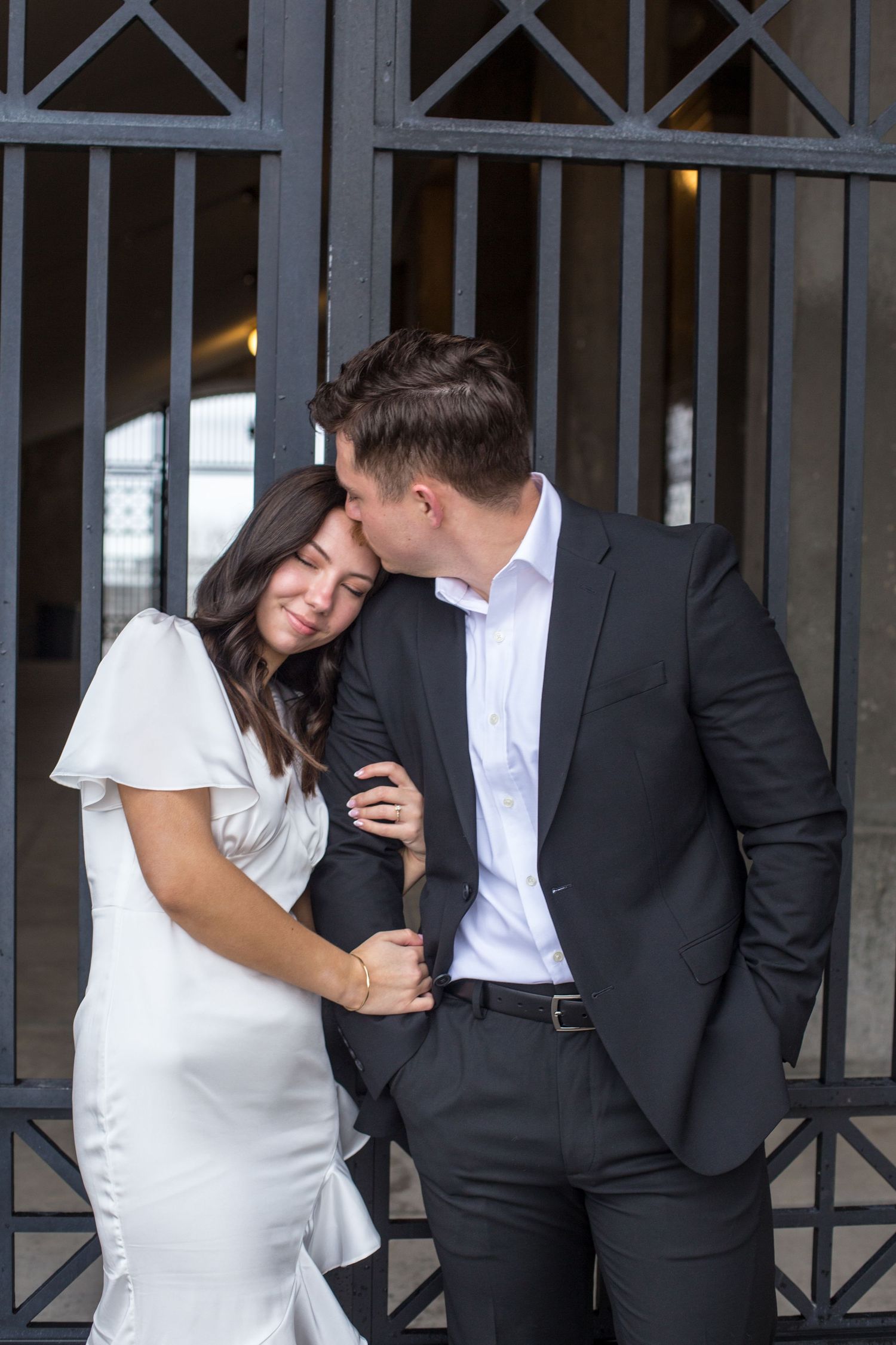 A couple in formal attire shares an intimate moment against an industrial doorway.