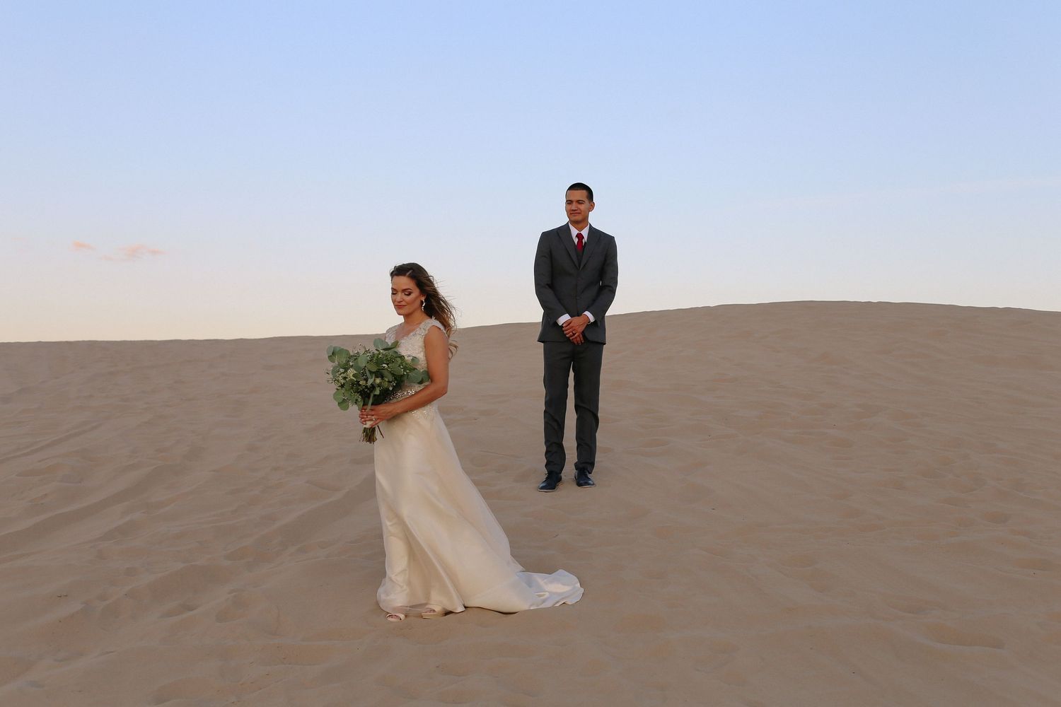 Wedding couple embraces while standing on sand dunes during golden hour photography session.