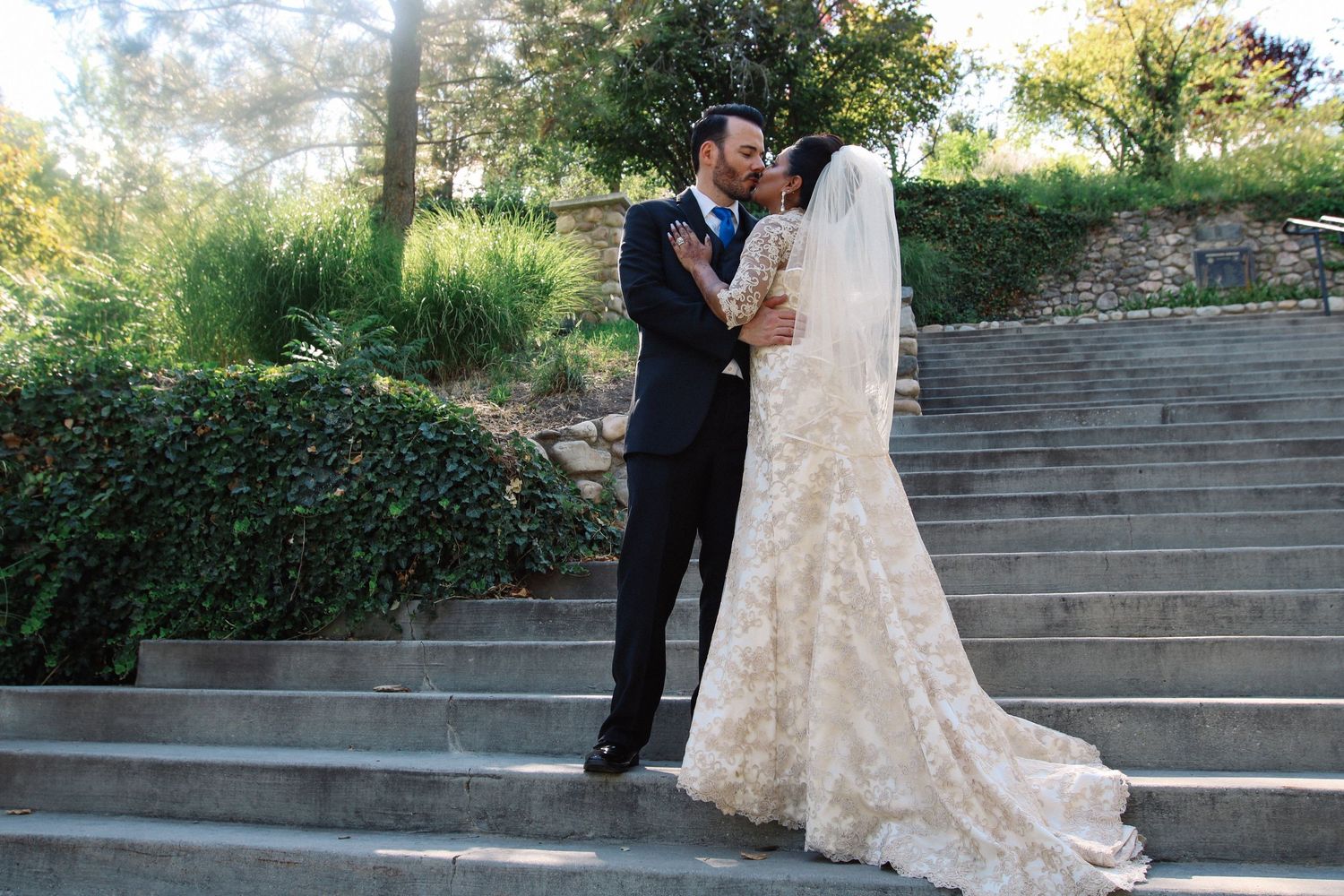 Wedding couple embracing on stone steps surrounded by greenery.