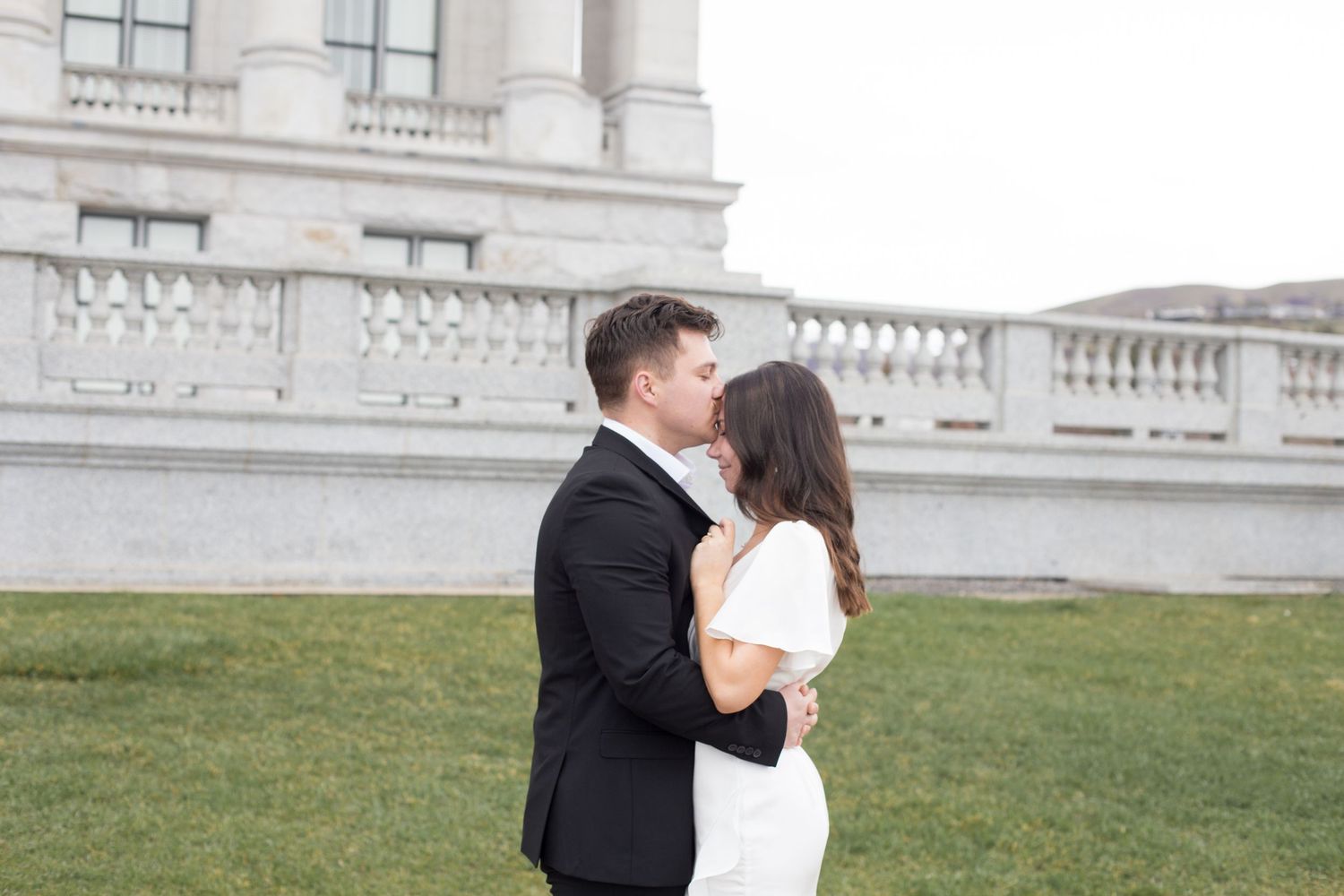 A couple embraces in formal wear against an elegant architectural backdrop.