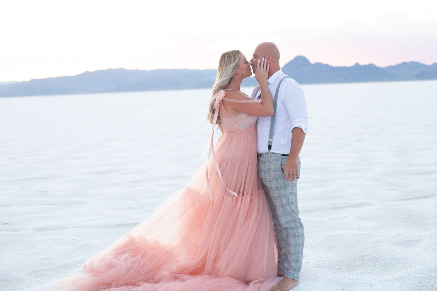 Intimate moment between couple on salt flats wearing formal attire at dusk.