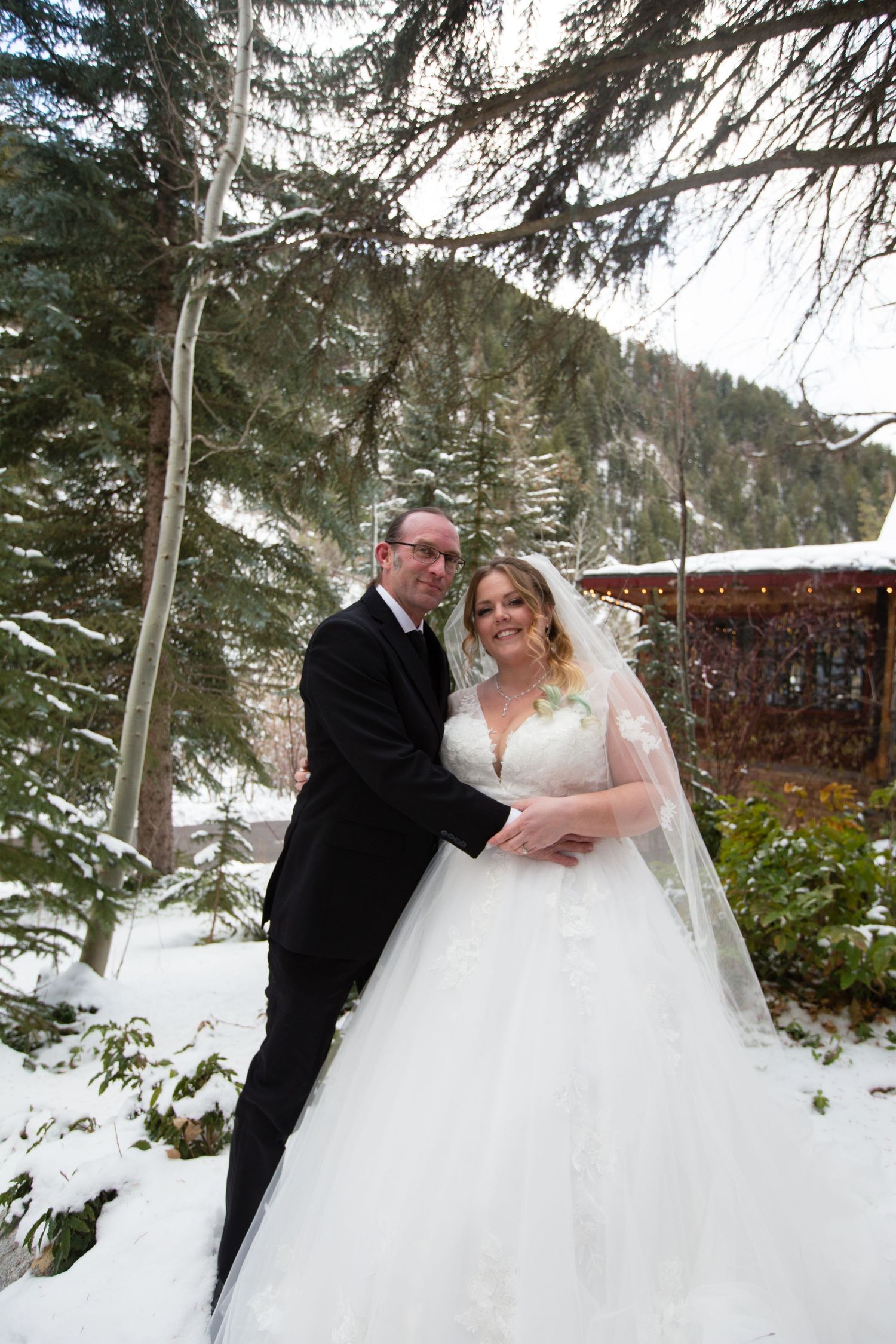 A beautiful winter wedding scene with newlyweds posing among snow-covered pine trees.