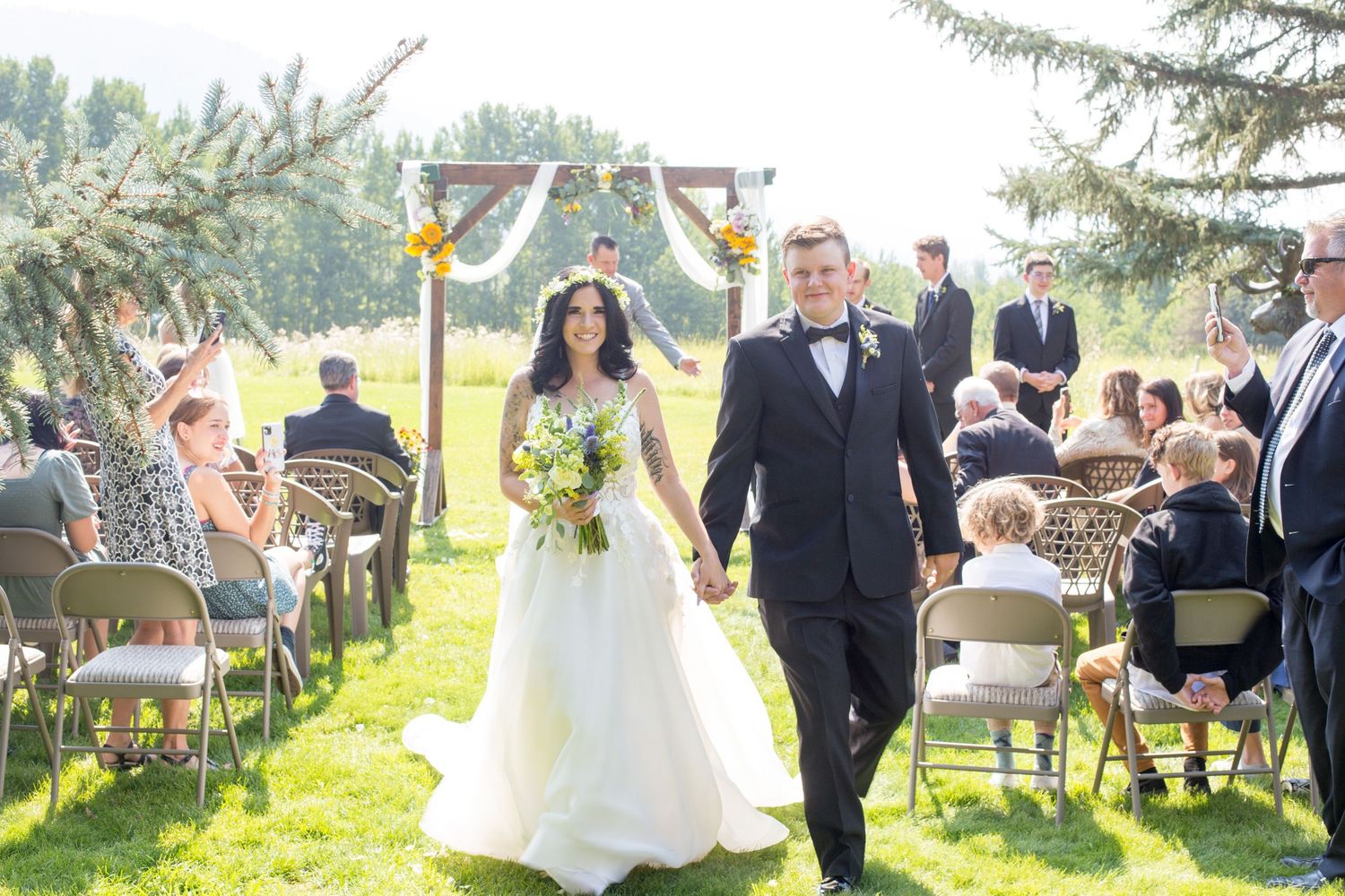 Wedding ceremony recessional on sunny lawn with guests seated on white chairs.