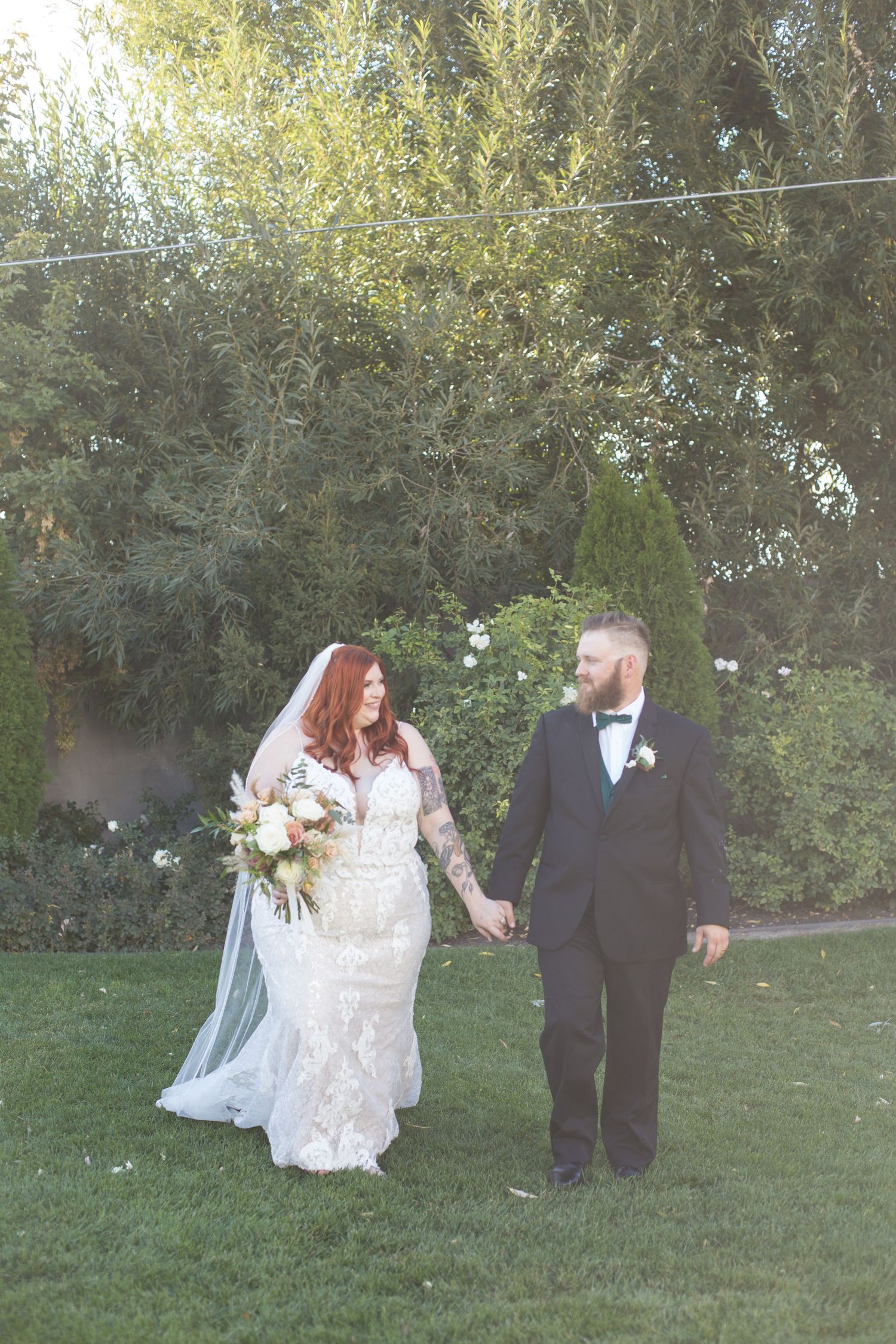 Wedding couple walking through green garden setting in formal attire with flowing white dress.