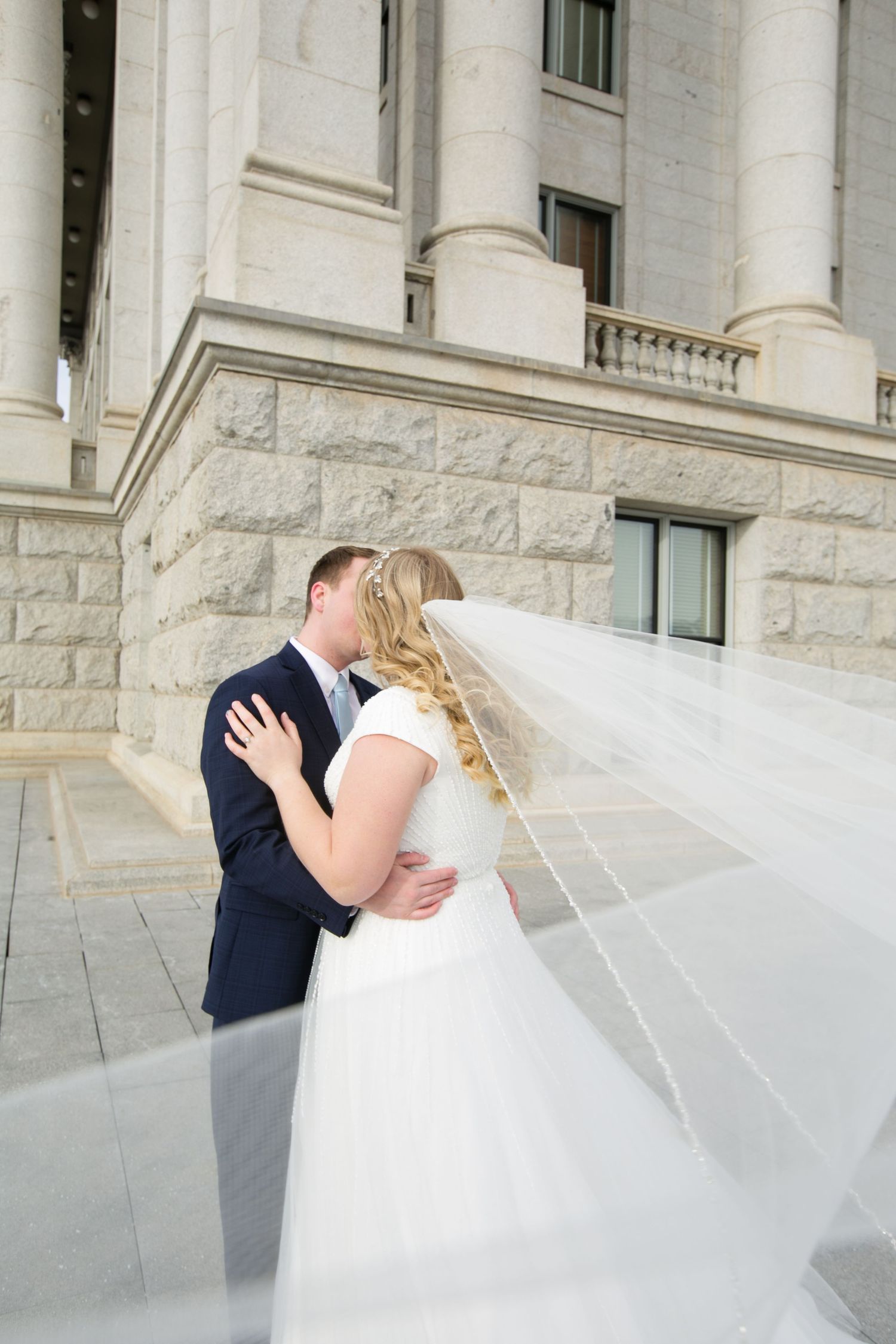 A romantic wedding moment captured in front of a grand stone building with classical columns.