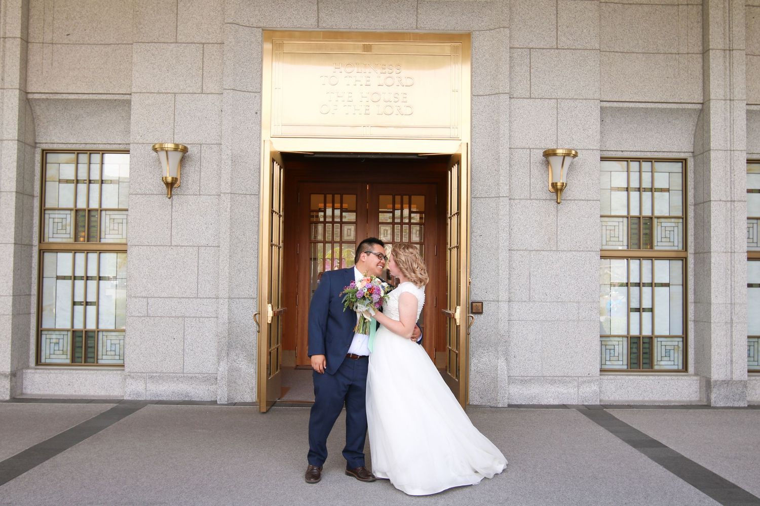 Wedding couple posing in front of a grand stone building with columns and windows.