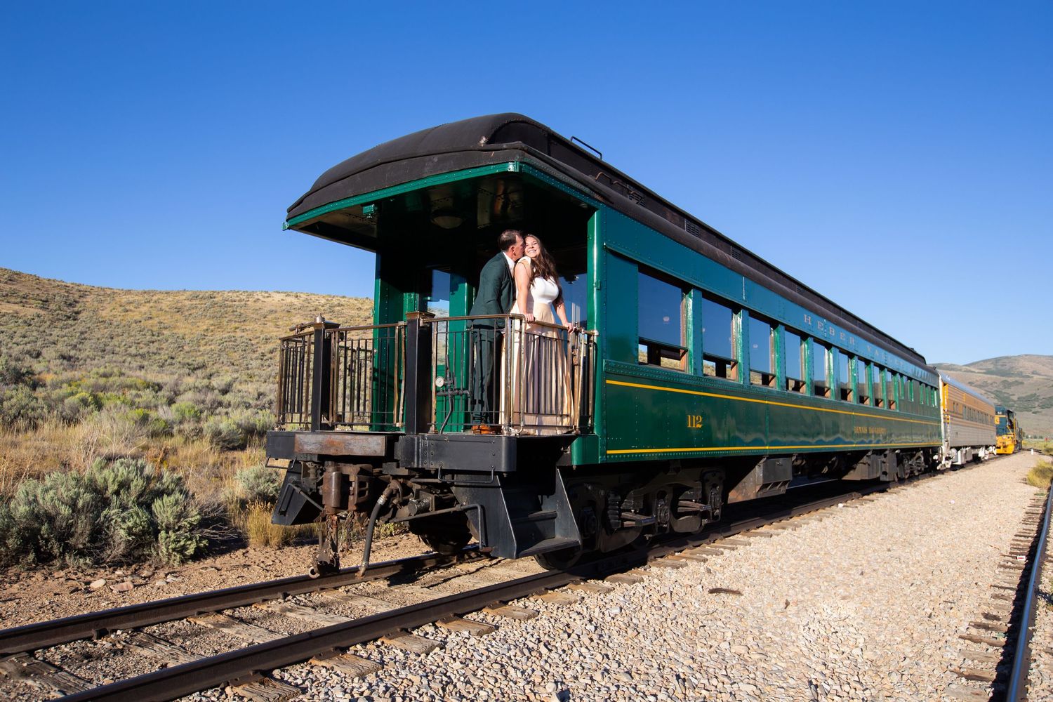 A vintage green passenger train car stationed in a desert landscape.