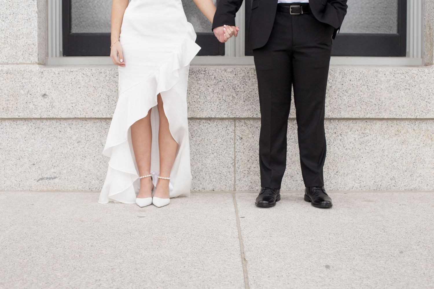 Playful wedding couple poses between architectural columns in black and white attire.