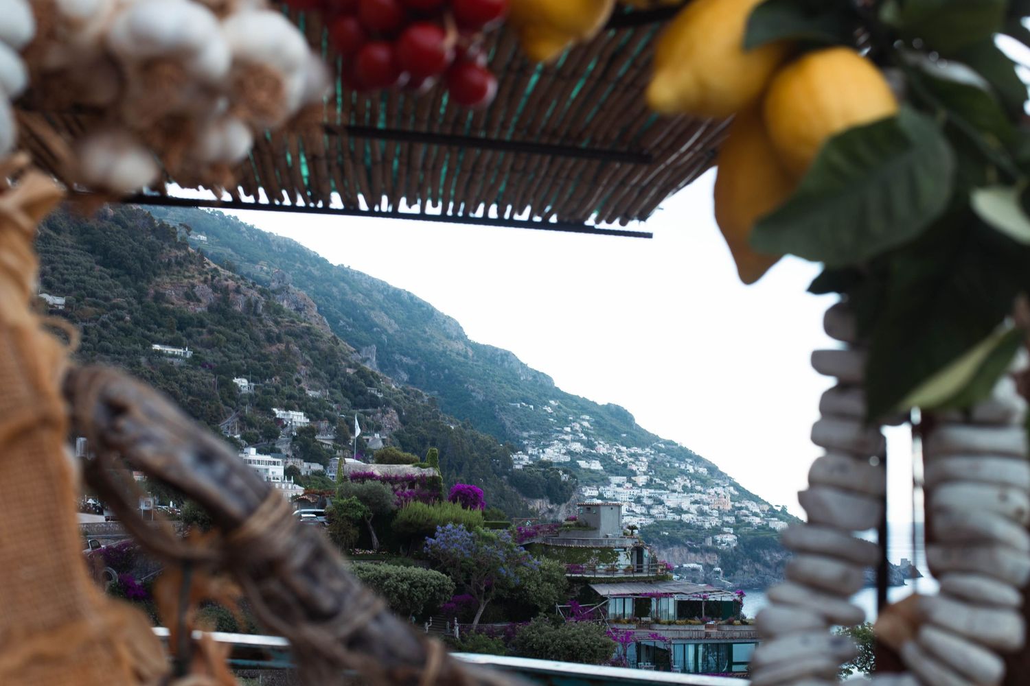 Scenic Positano hillside village framed through hanging garlic, lemons and shells decoration.