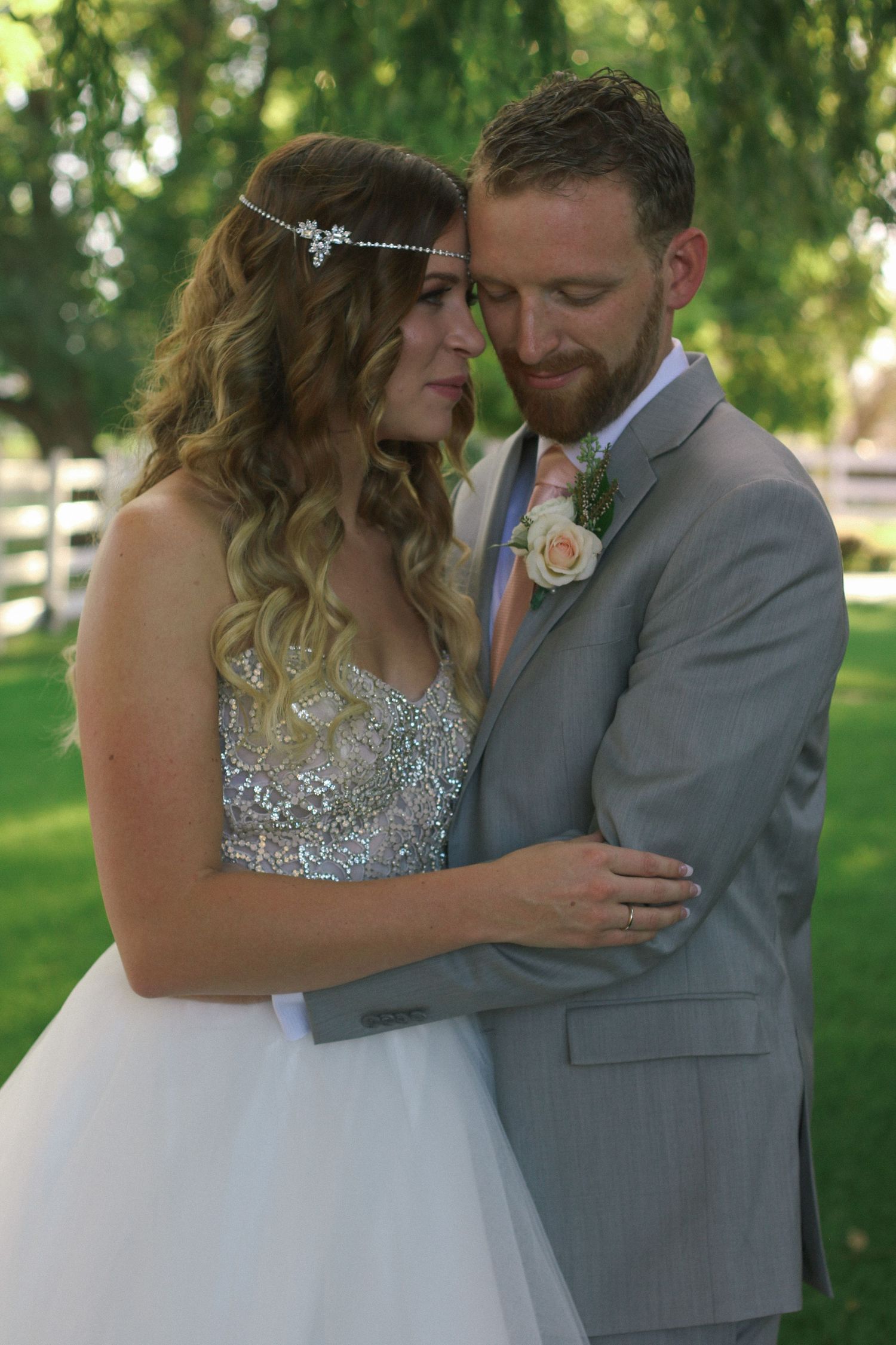Intimate wedding portrait under trees with bride in sparkly dress and groom in grey suit.