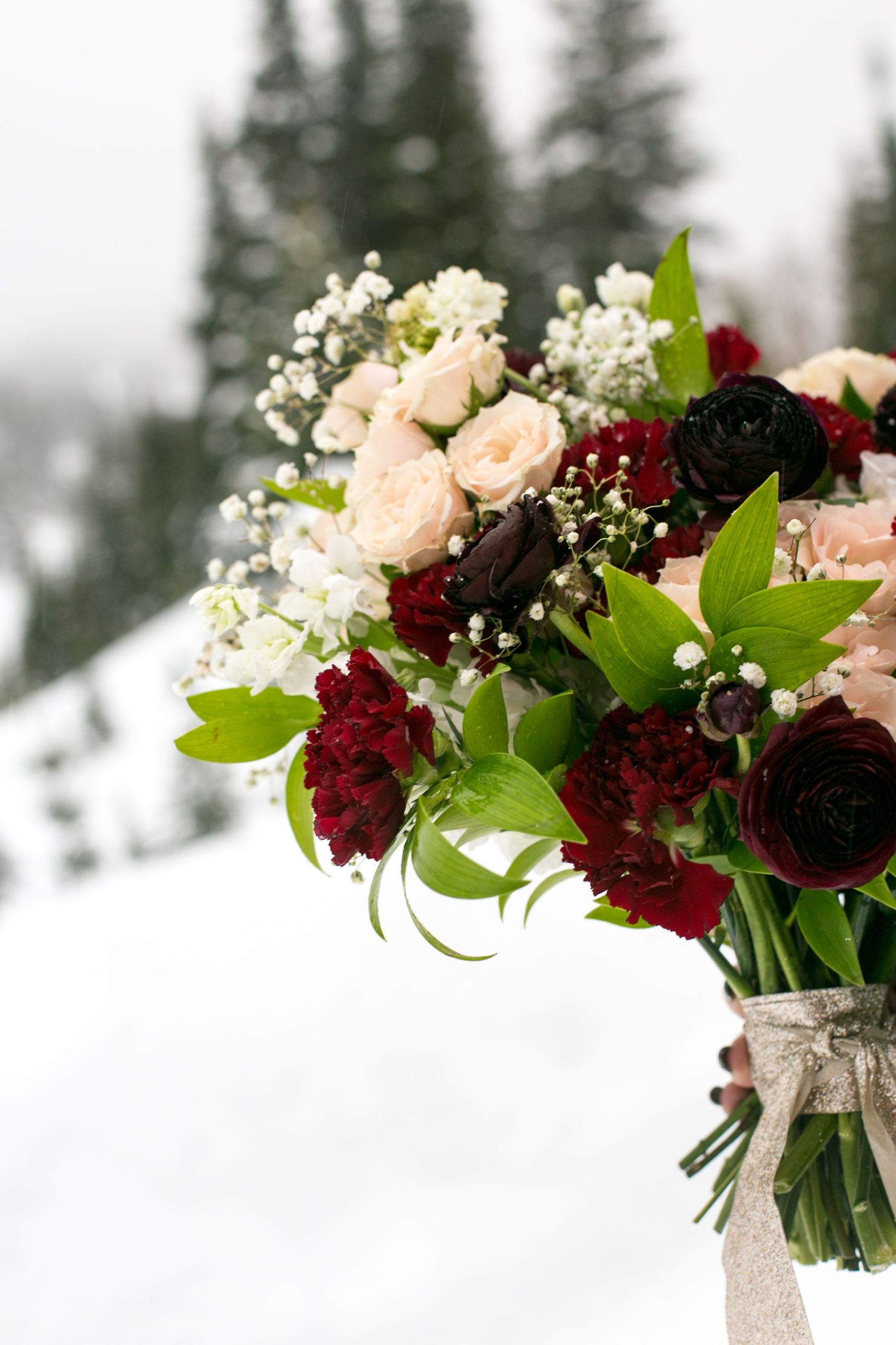 Elegant floral arrangement with burgundy and blush roses against snowy background.