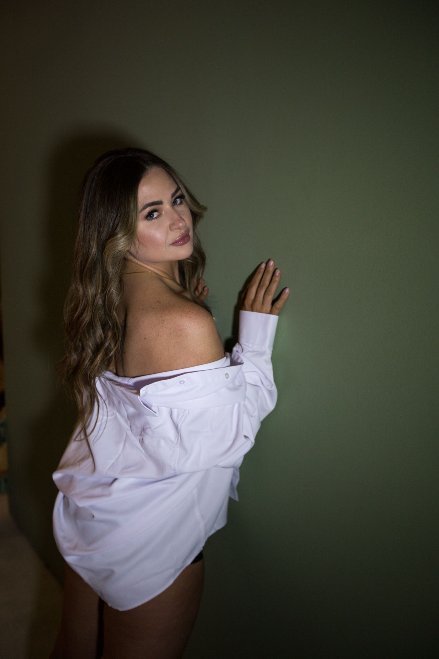 Dramatic portrait series featuring white off-shoulder top against dark green wall.
