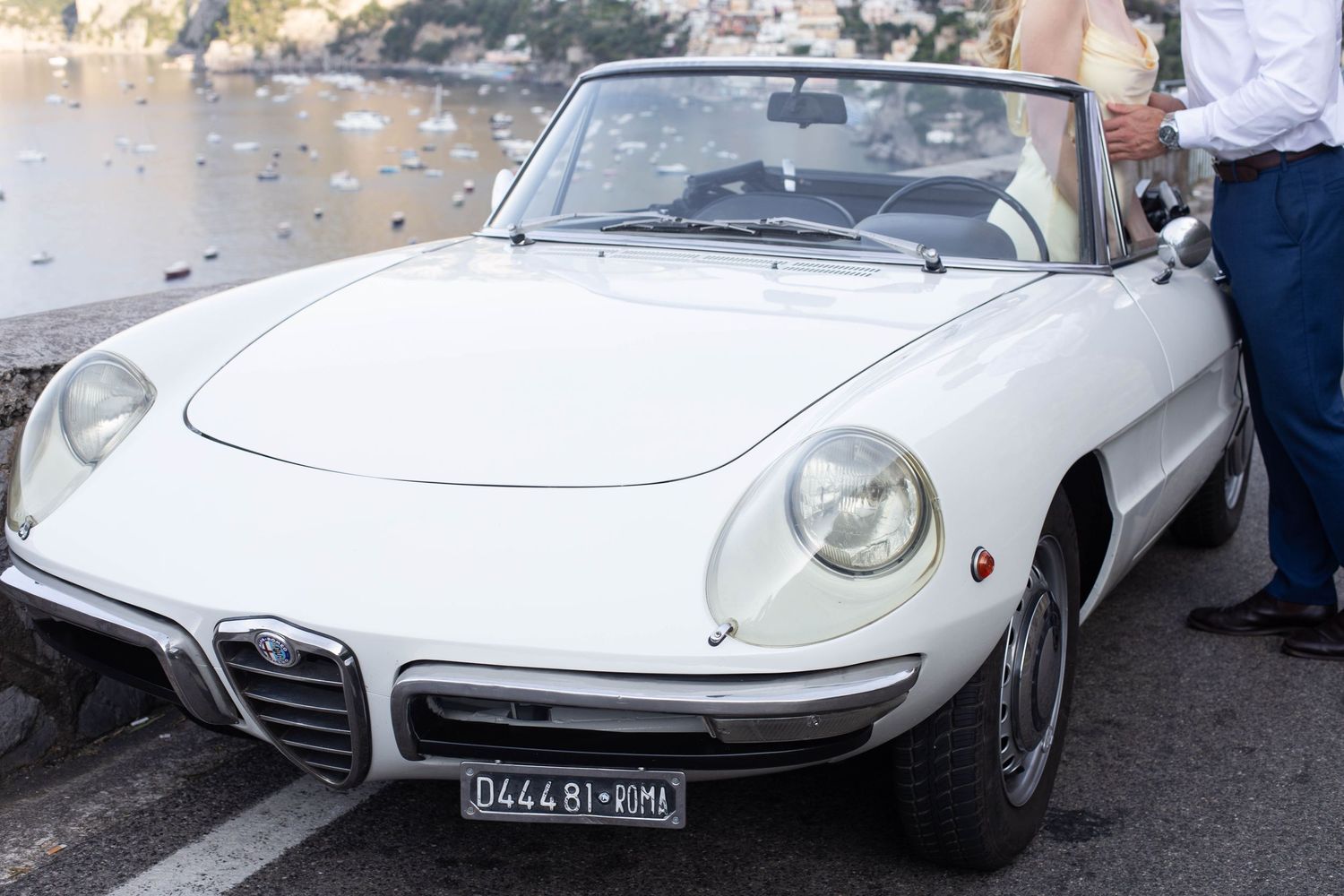 Classic white Alfa Romeo Spider convertible with Italian license plate parked on the Amalfi Coast.