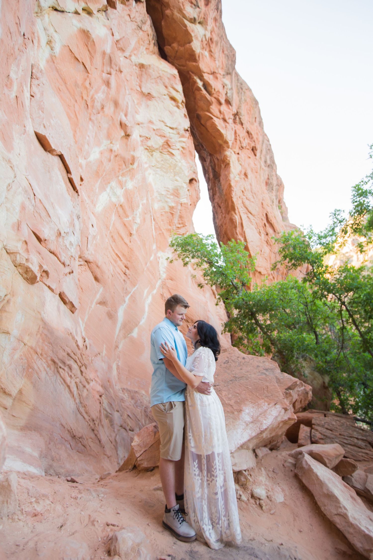 Couple posing against dramatic red rock formations in natural canyon setting.