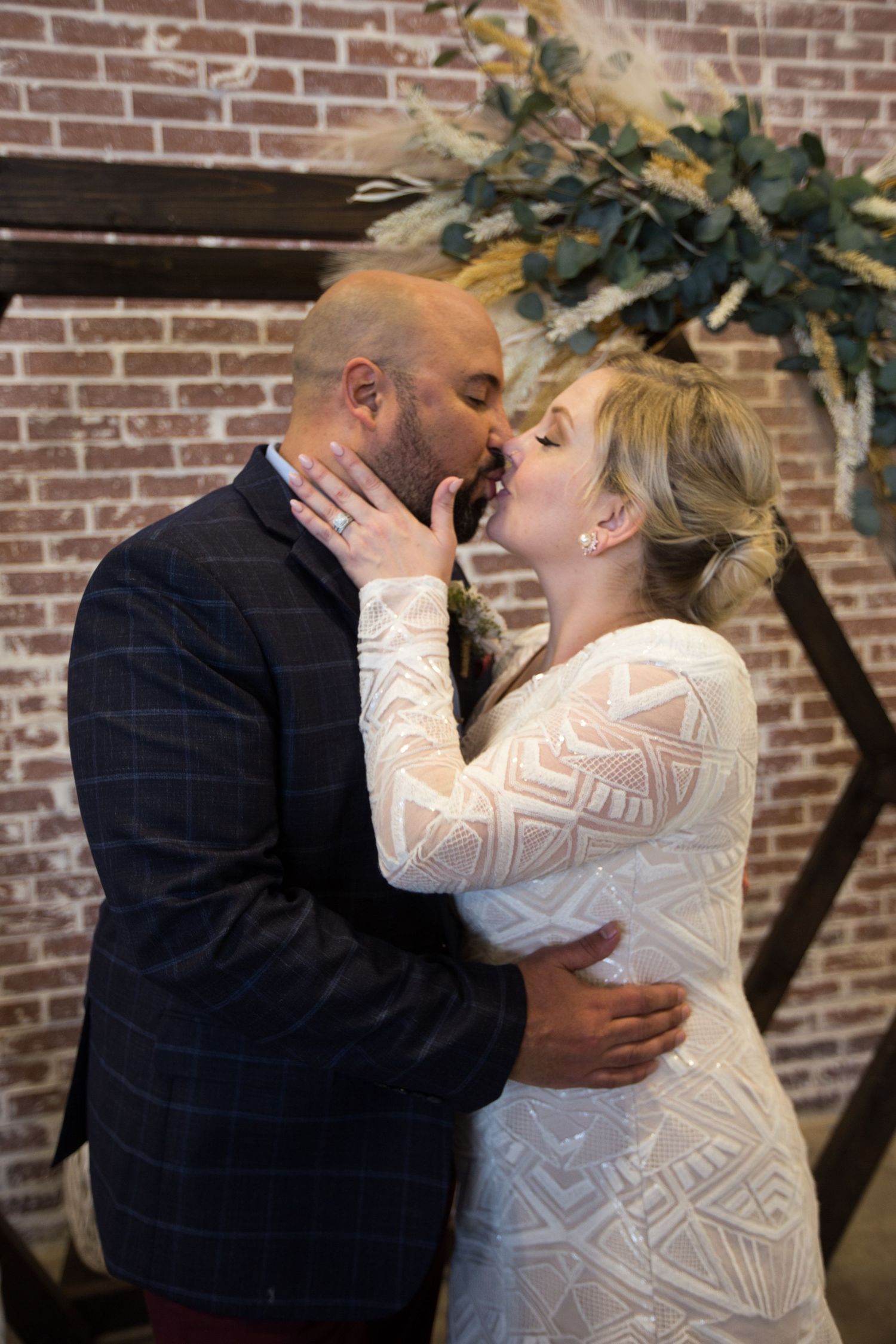 Intimate wedding moment against brick wall with decorative greenery arch.