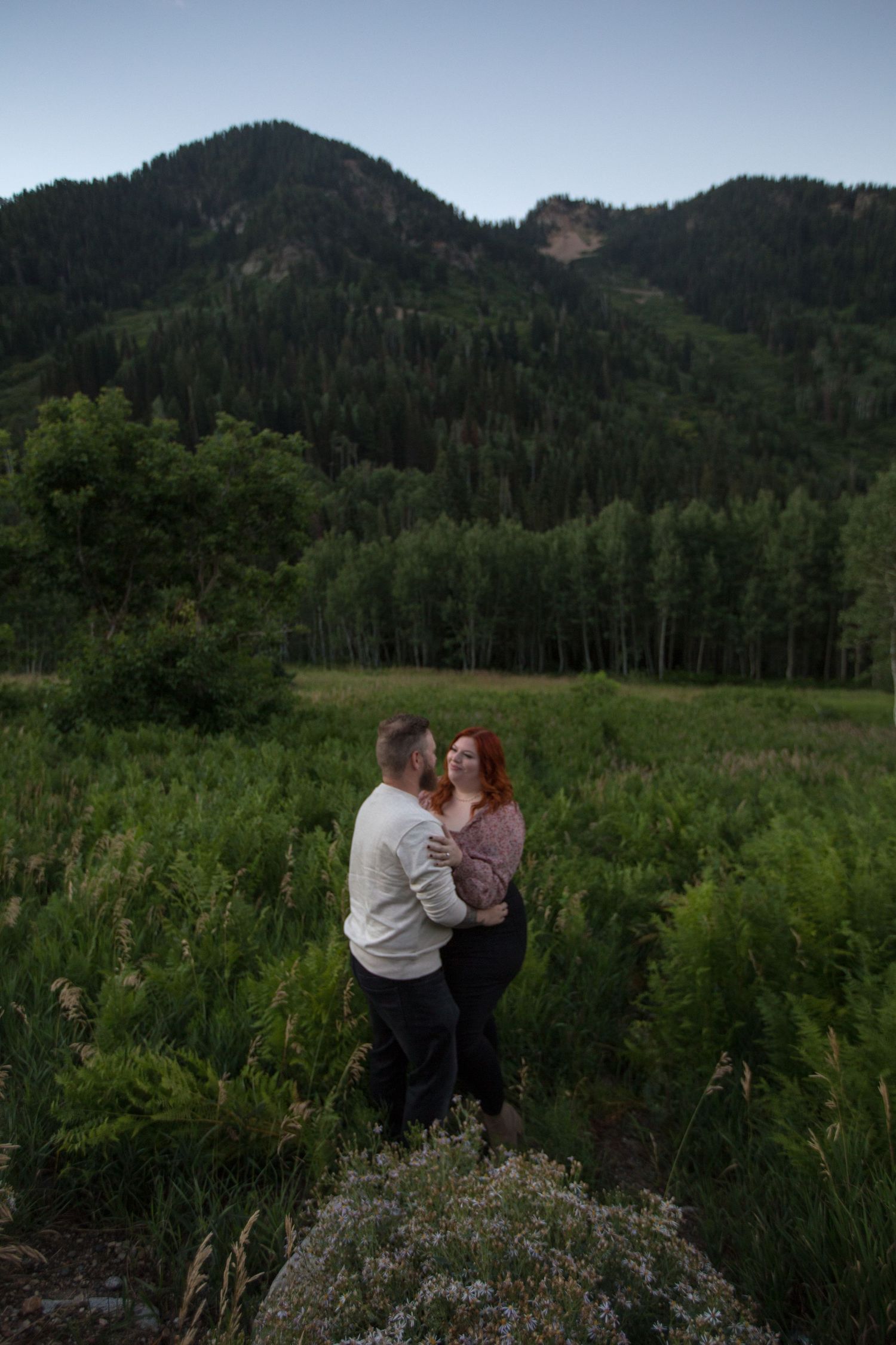 A couple shares an intimate moment against a backdrop of mountain scenery and wildflowers.