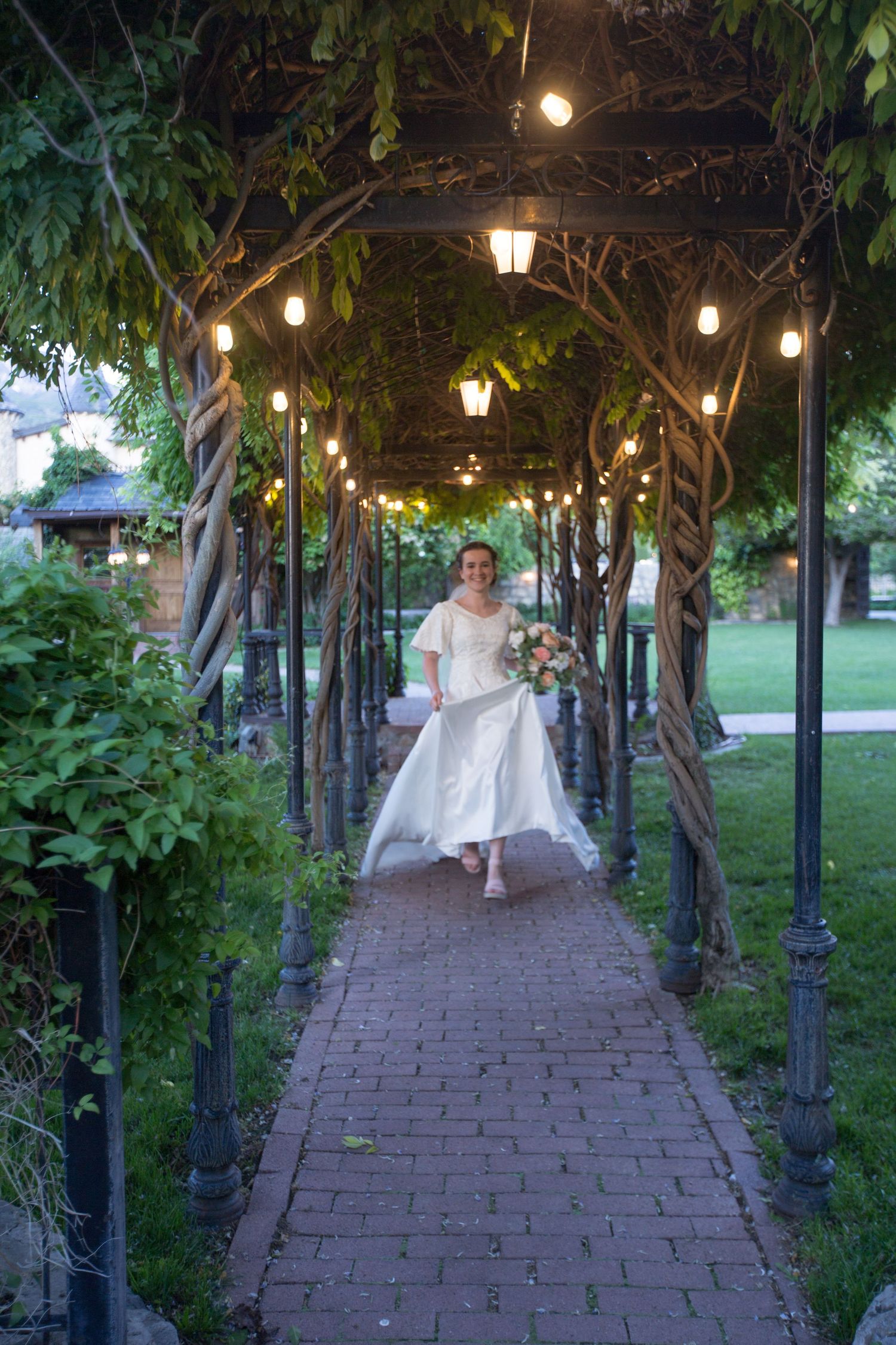 A garden walkway with string lights and vines creating a romantic tunnel effect.