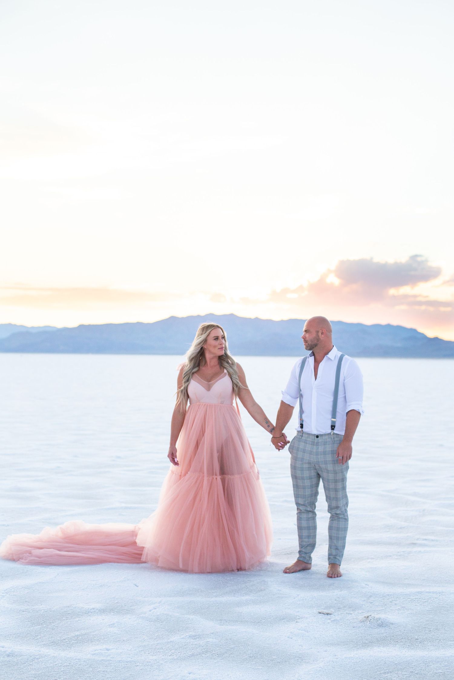 Wedding couple poses on white salt flats in pink gown and grey suit.