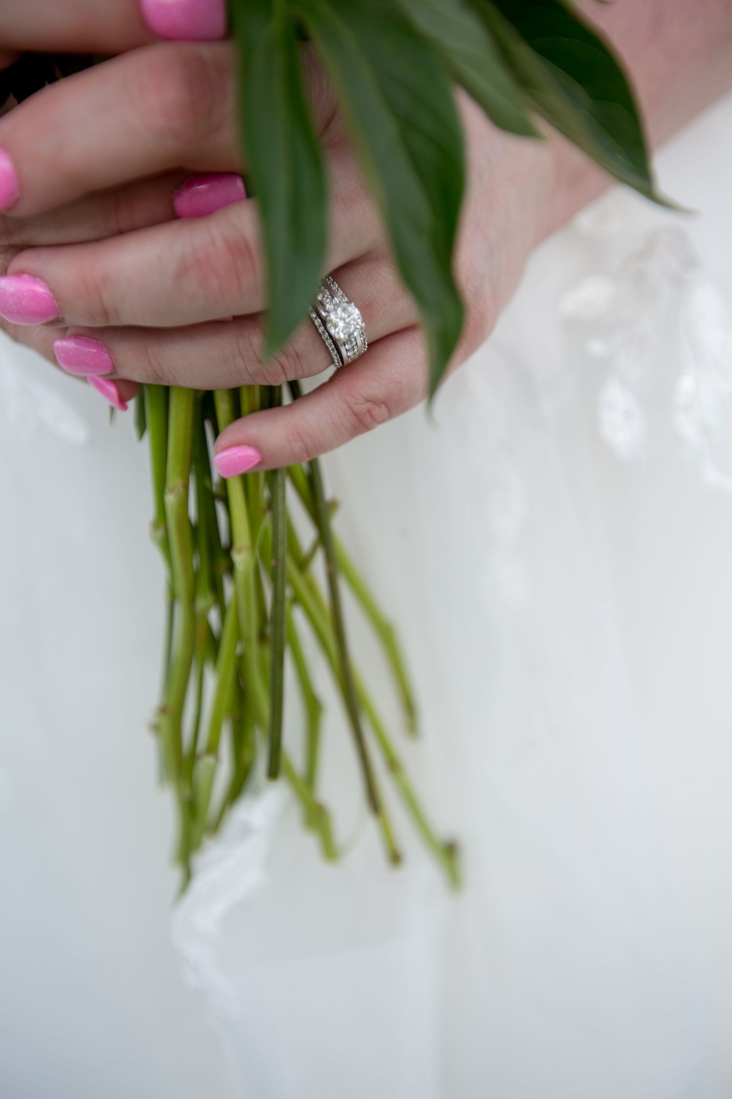 Close-up of hands holding a bouquet stem with pink nails and sparkling engagement ring.
