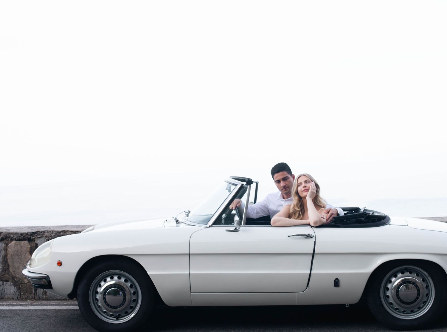 Romantic couple sitting together in white vintage convertible on the scenic Amalfi Coast road.