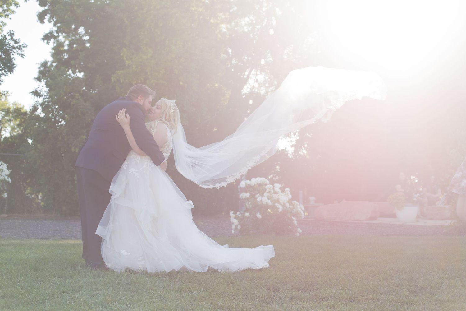 A couple in wedding attire sits on grass during sunset.