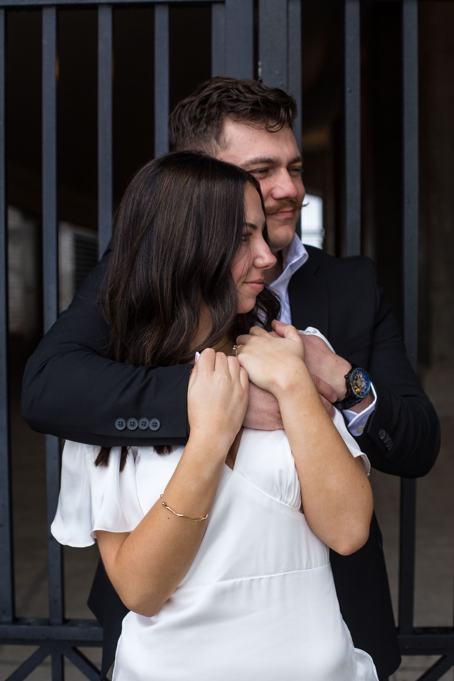 Tender moment between couple in formal attire near industrial gates.