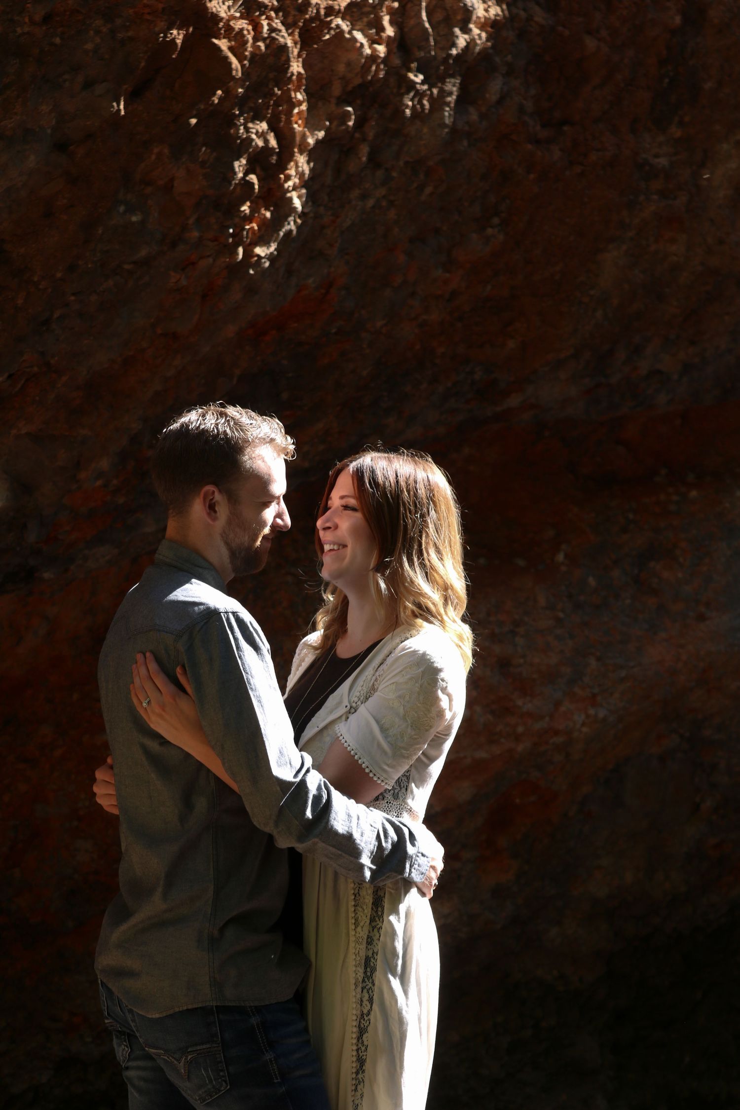 A romantic couple embraces against a dark textured wall with dramatic lighting creating an intimate mood.