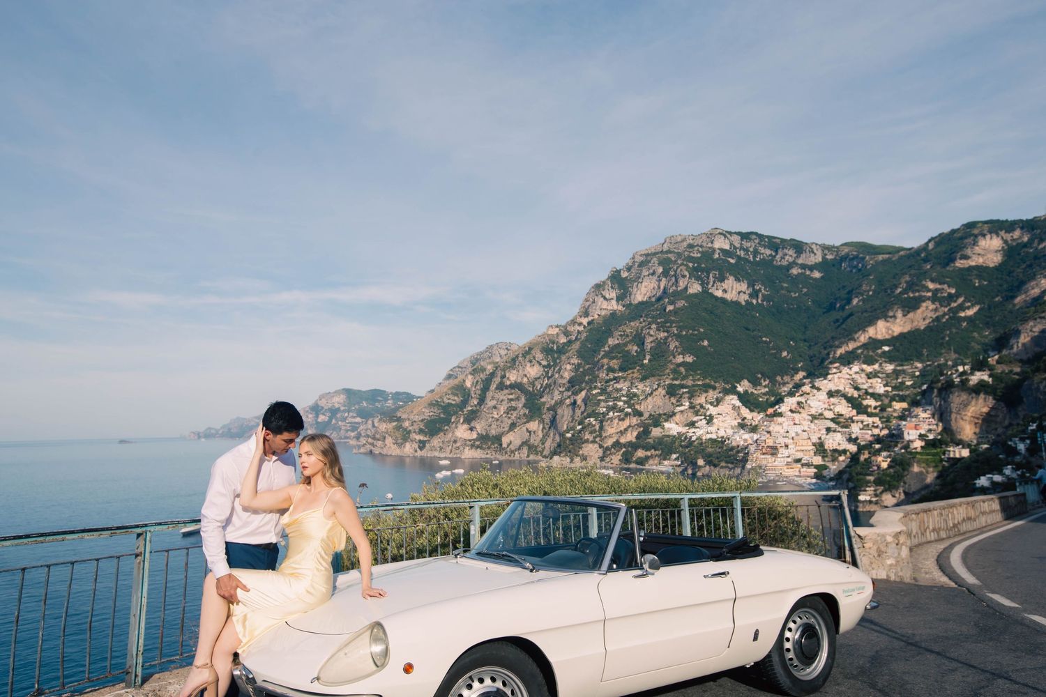 Couple posing with white vintage convertible on Amalfi Coast overlook with breathtaking sea views.