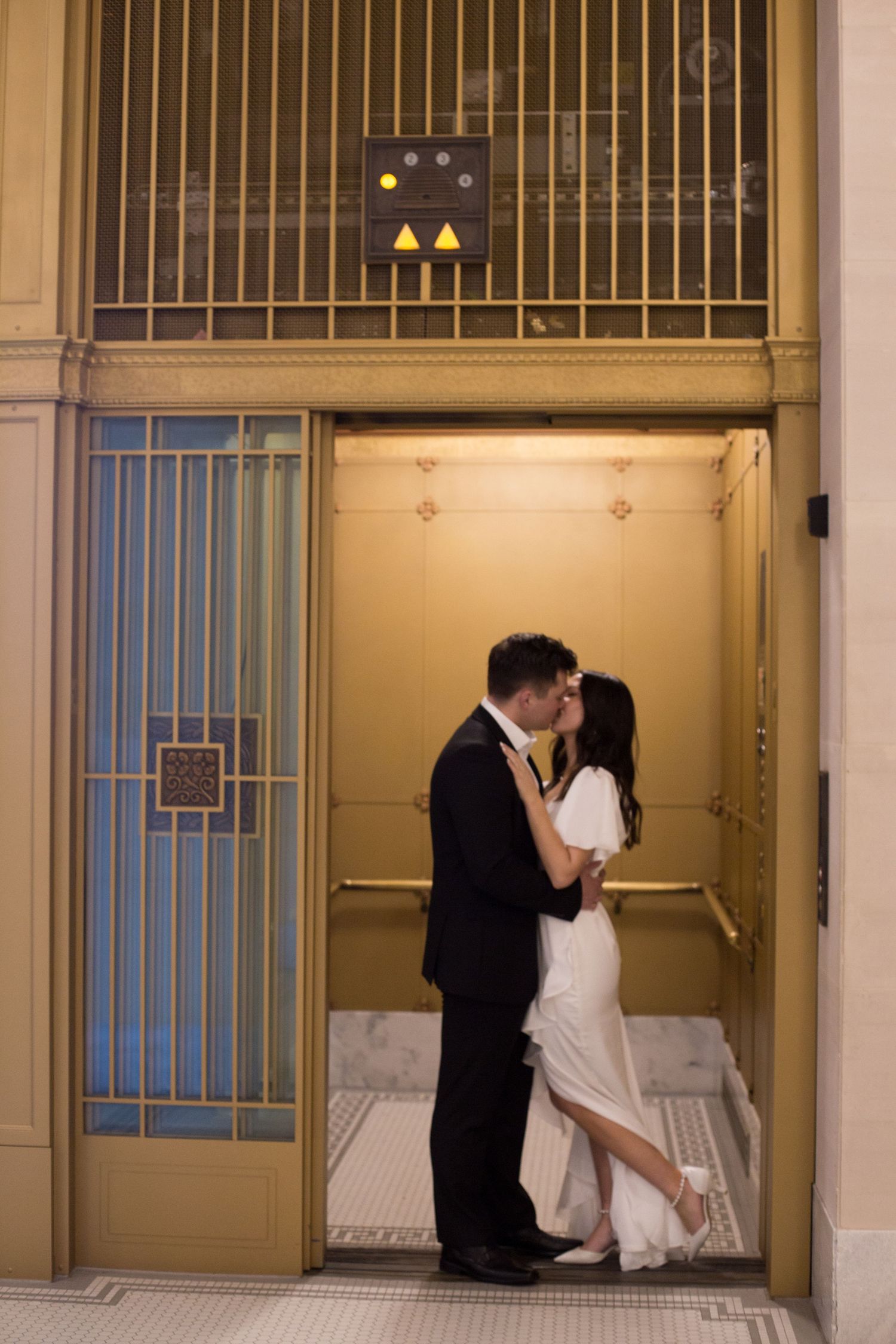 A romantic moment shared in a vintage elevator with gold metallic gates and art deco details.