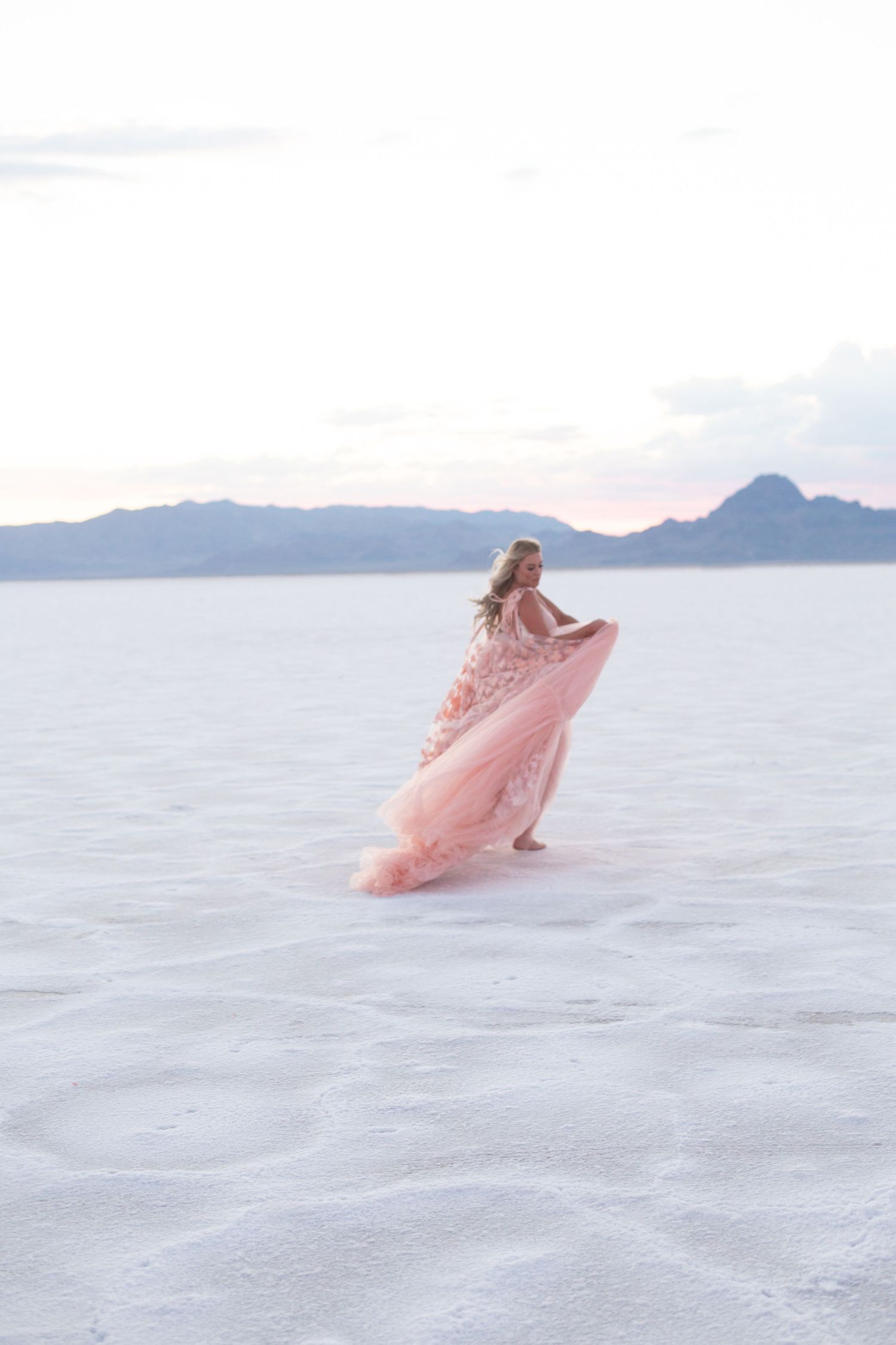 Pink tulle dress flows gracefully across pristine white sand with mountains in the distance.