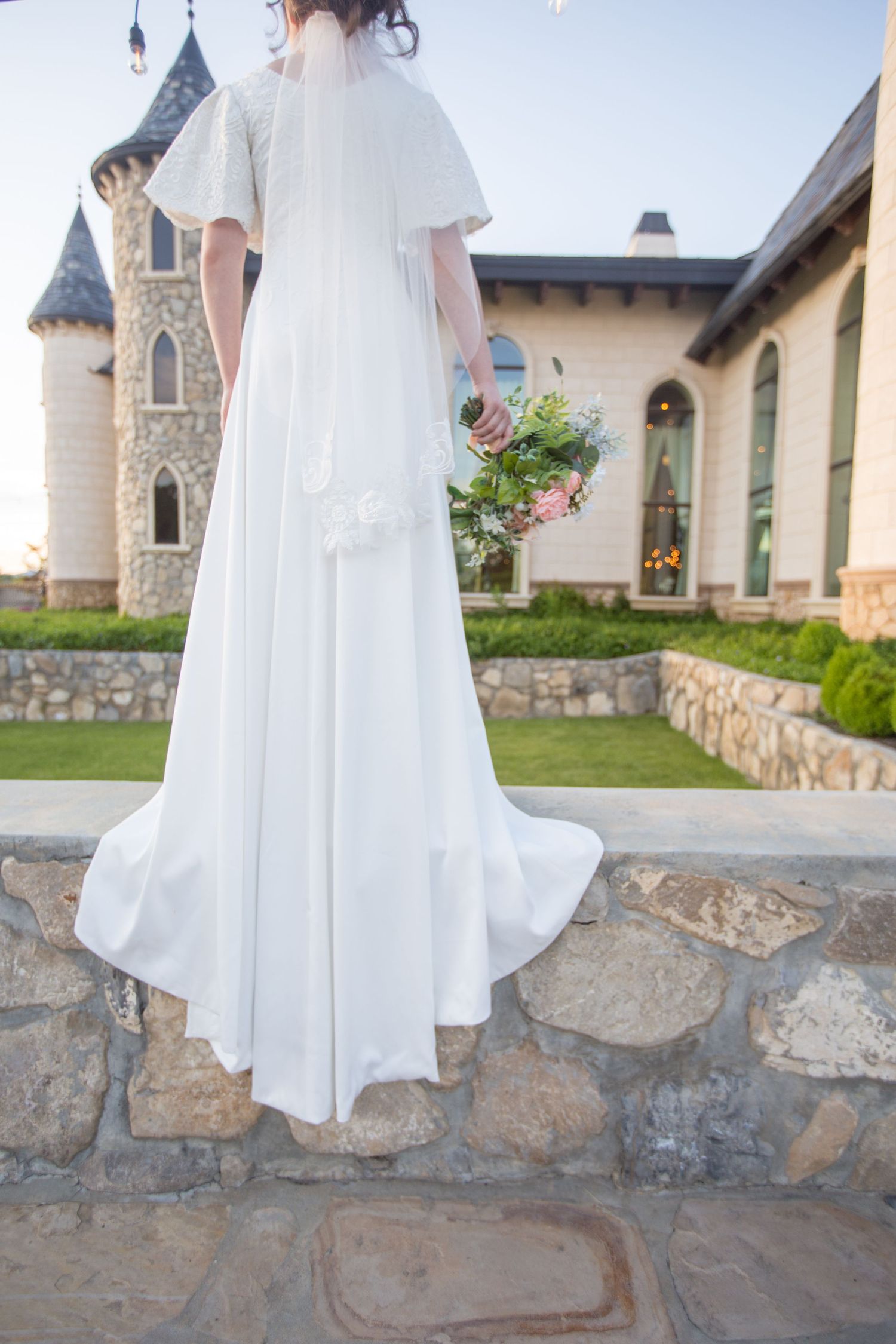 A white wedding gown photographed against rustic stone walls and castle architecture.