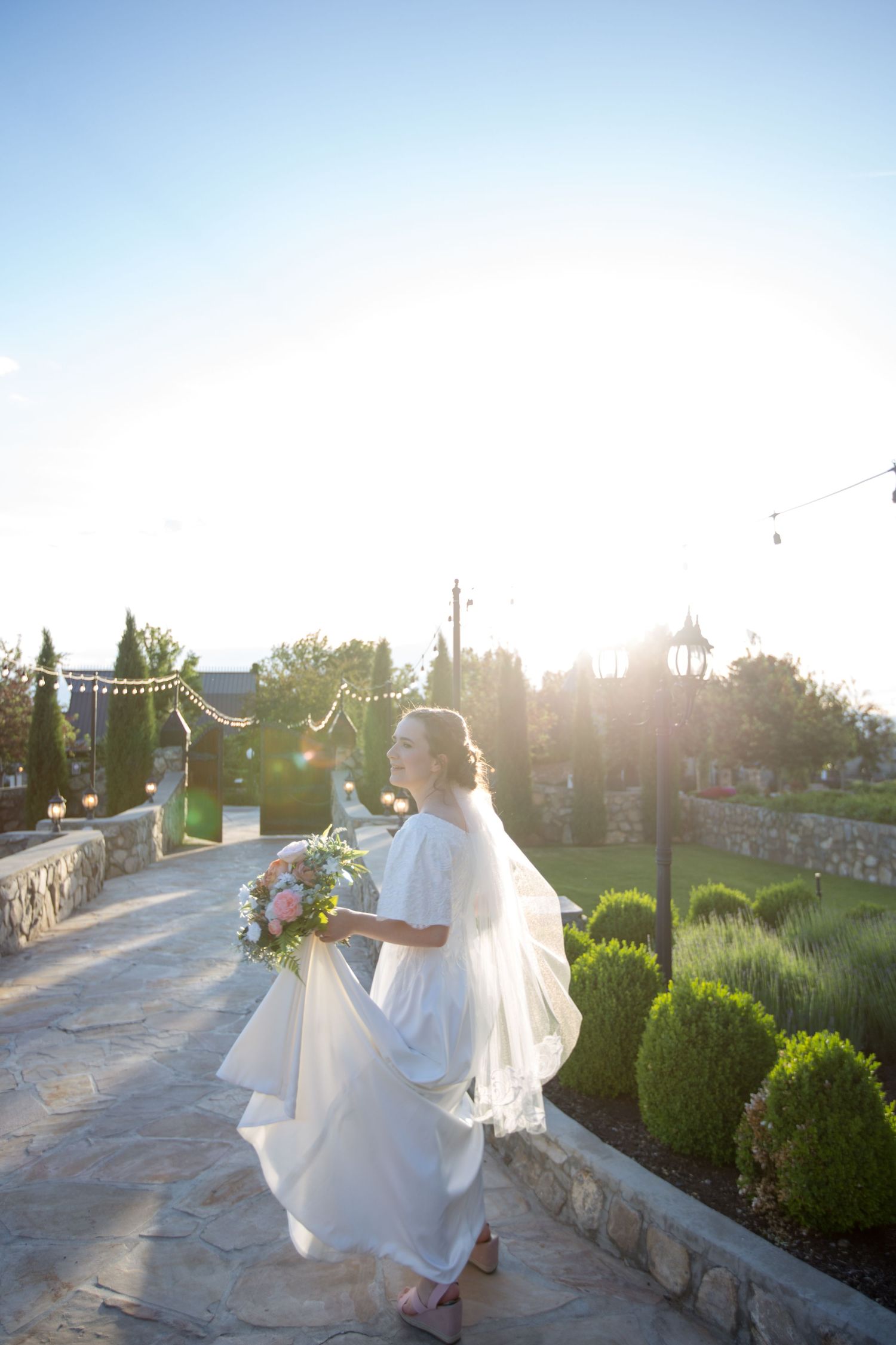 Sunset bridal portrait on stone pathway with string lights and garden scenery.