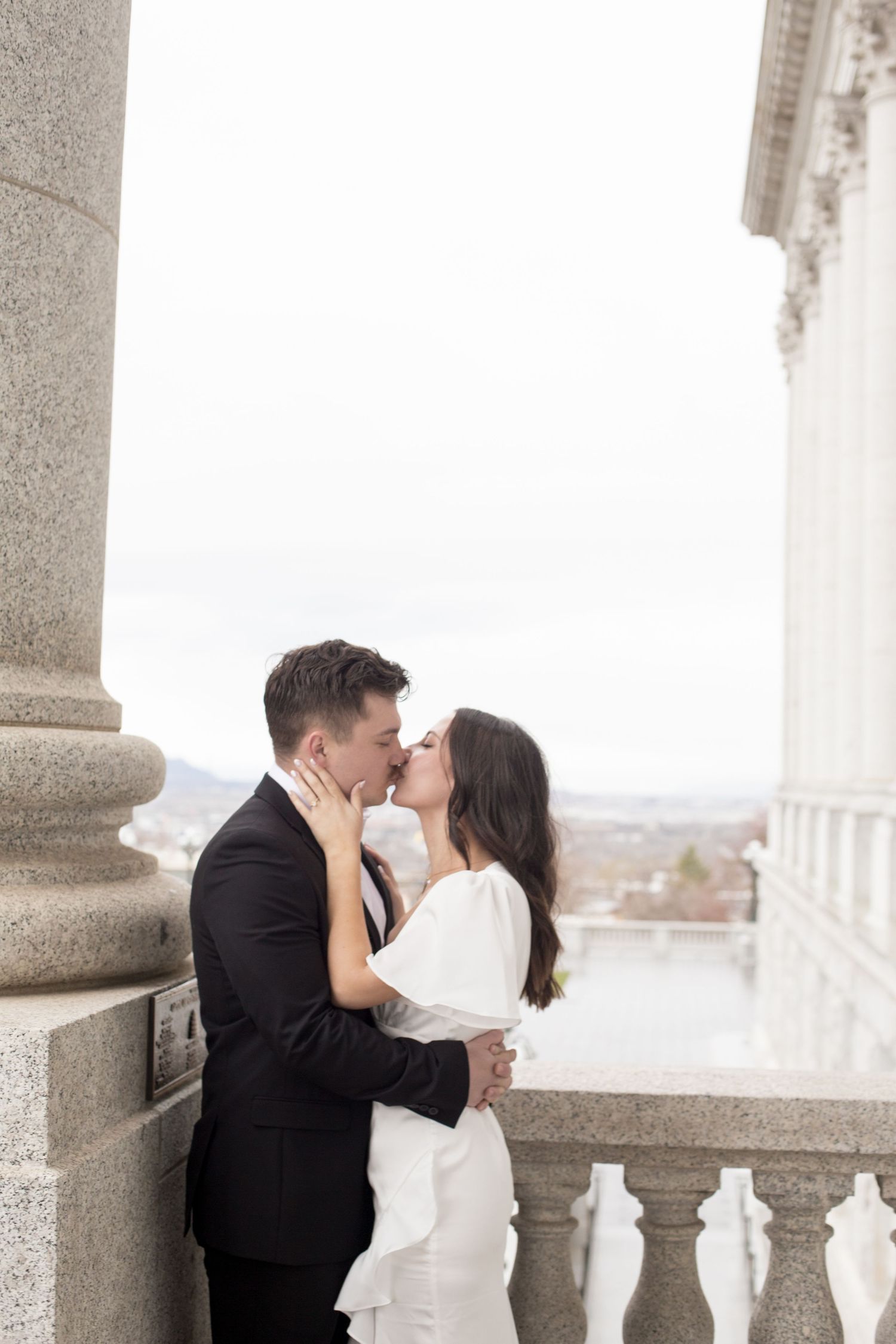 A romantic moment shared between newlyweds on a columned balcony overlooking a scenic view.