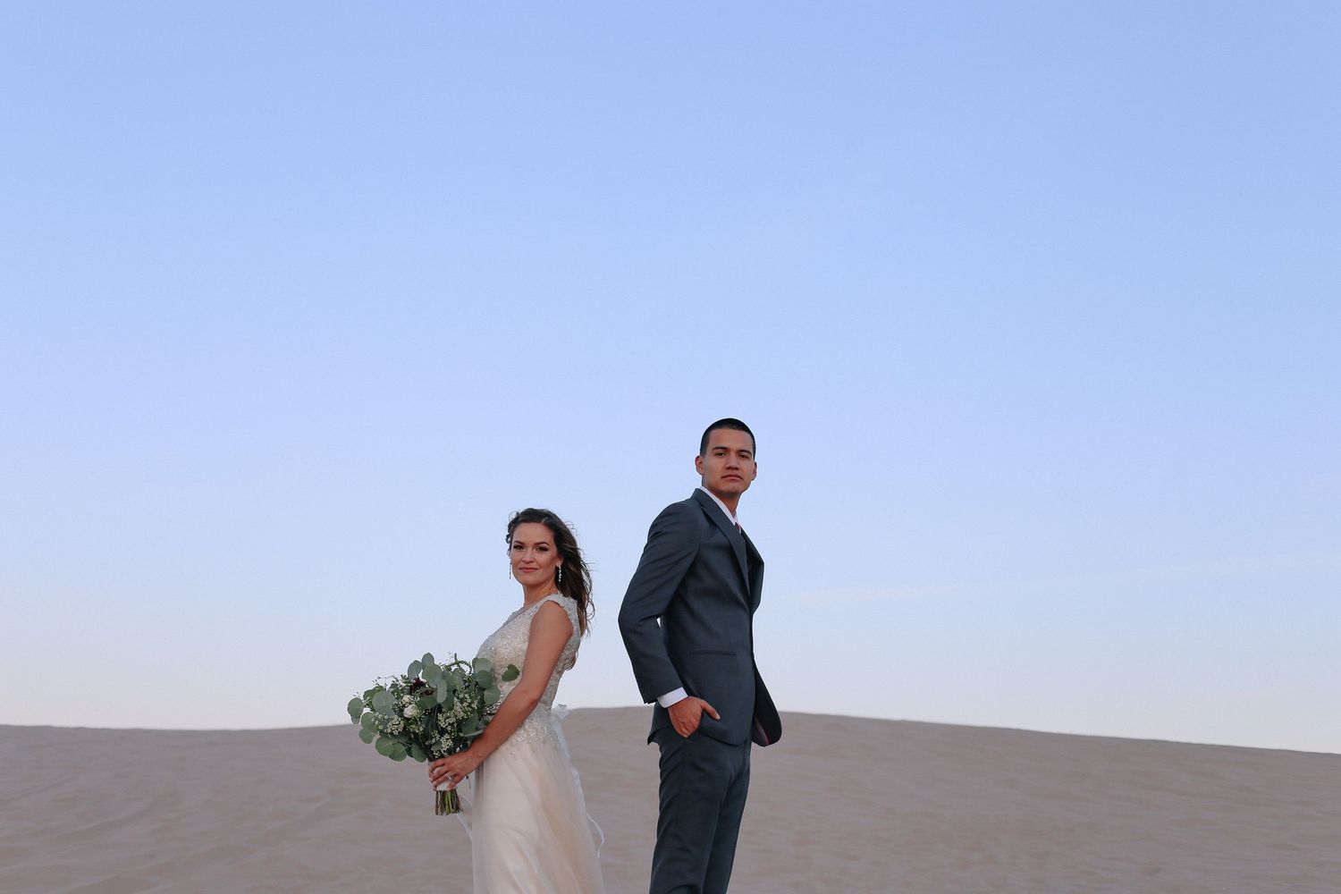 Newlyweds pose for romantic photos in a desert landscape at sunset.