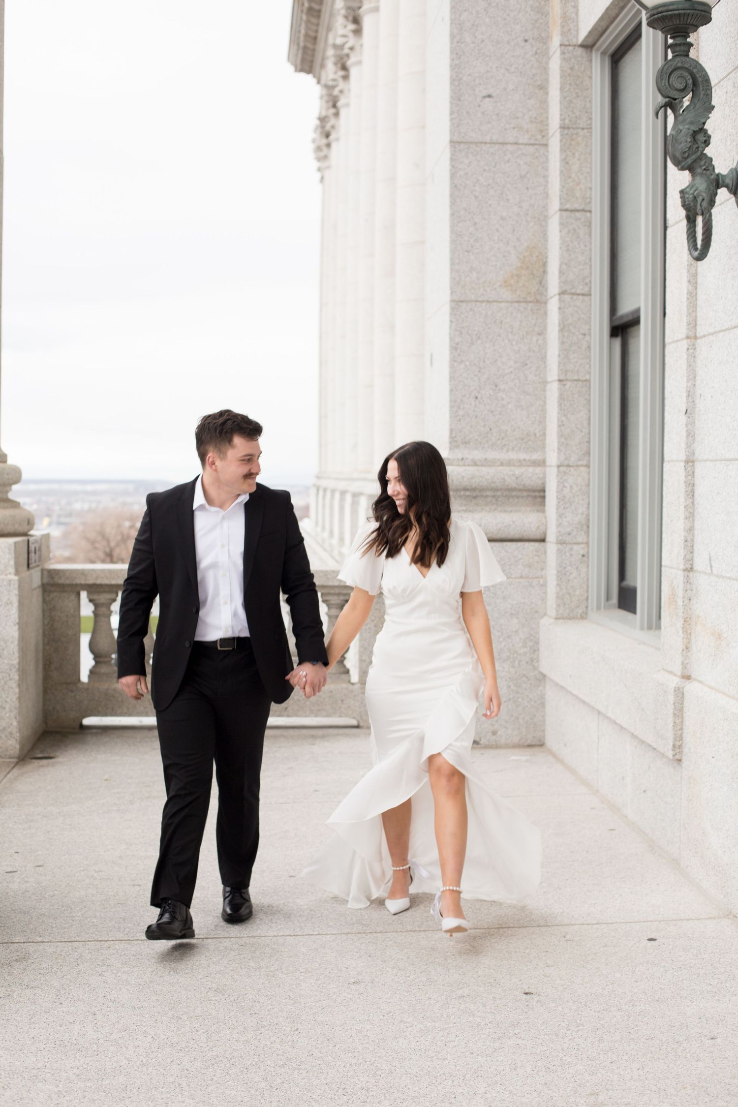 Couple walking along elegant columned building exterior in formal attire.