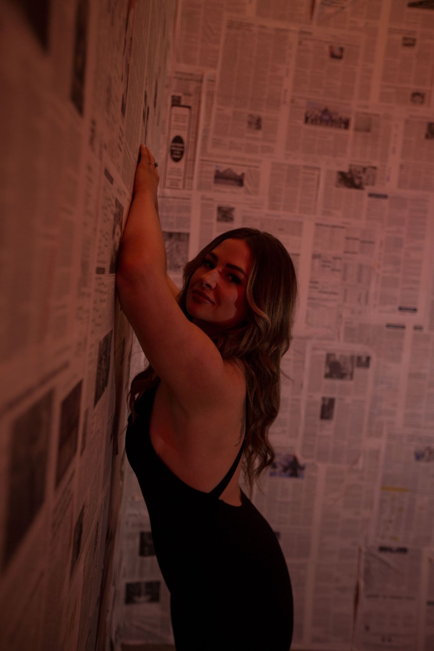 Dramatic pose against wall covered in newspaper clippings.