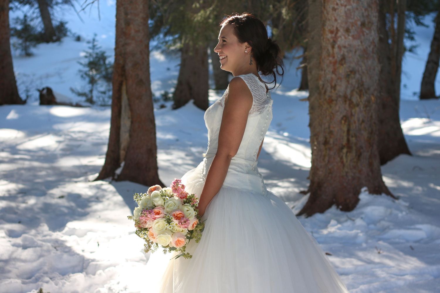 A bride in a flowing white dress poses against a snowy winter forest backdrop.