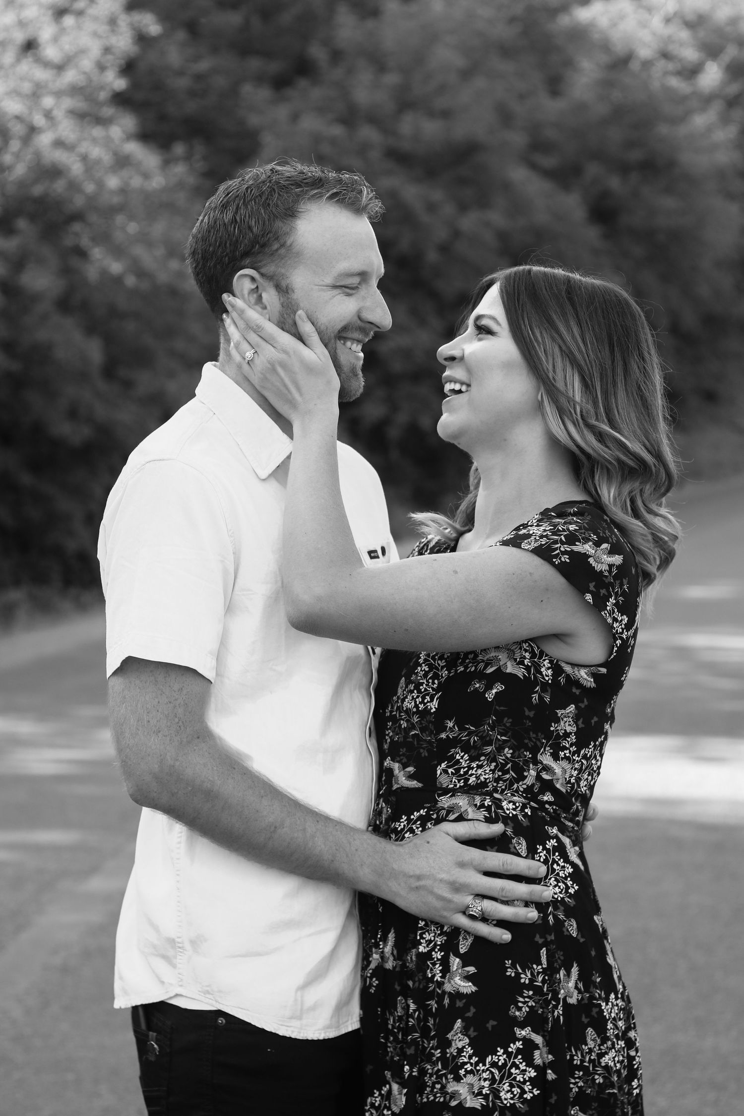 Happy couple embracing outdoors in black and white photo, woman touching mans face lovingly.