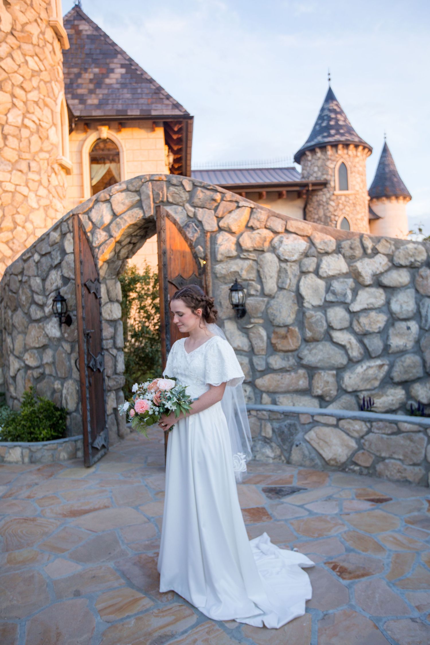 A white wedding dress photographed against a stone castle wall with turrets and arched doorways.