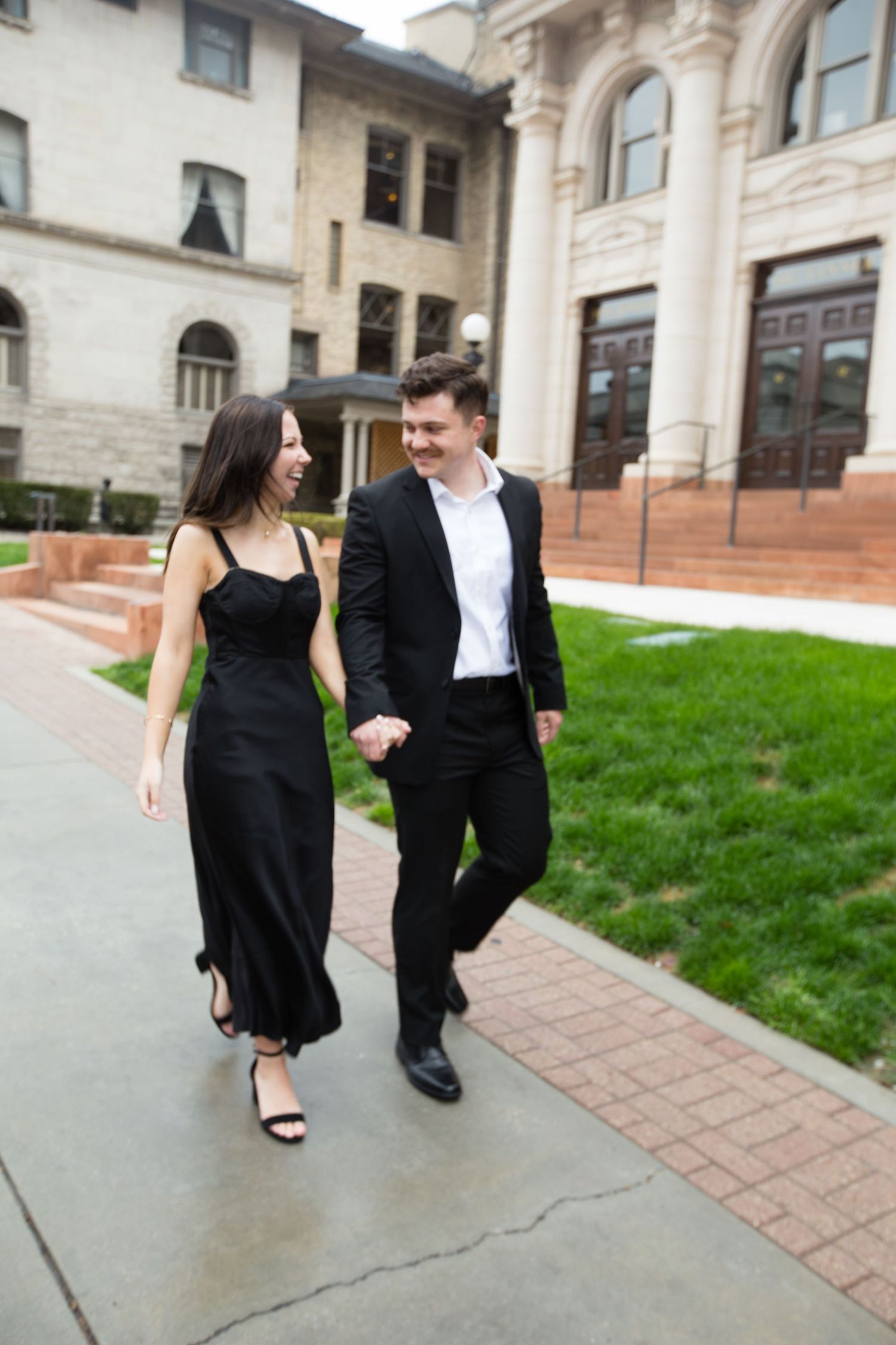 Couple in formal wear walking together along pathway by historic building.