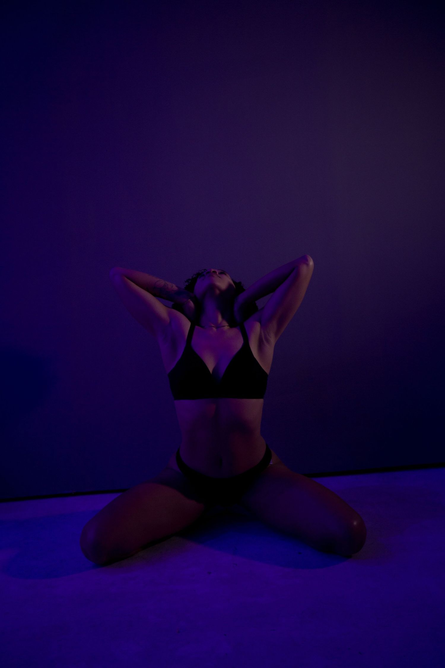 Figure in relaxed pose under dramatic purple lighting.