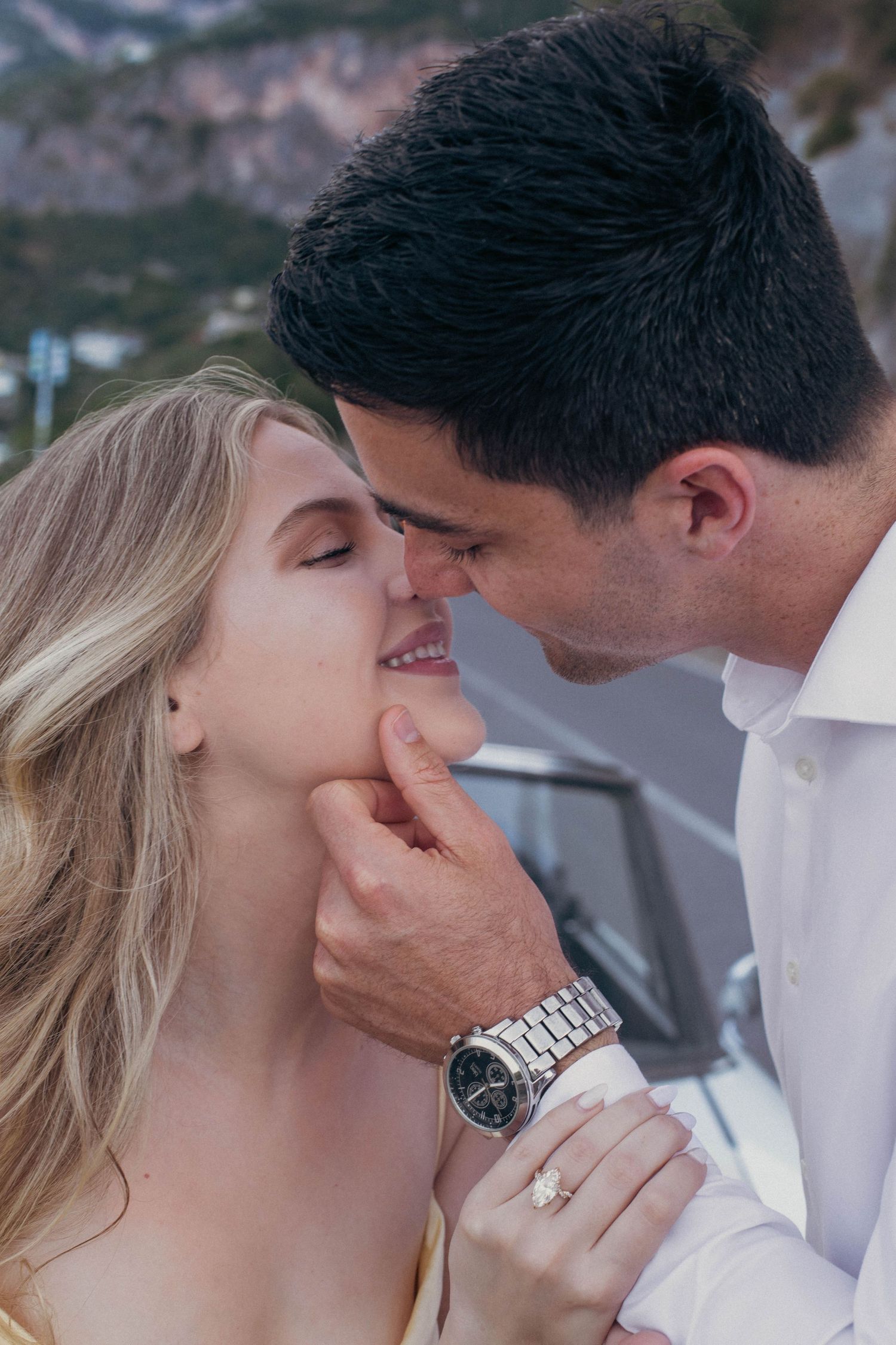 Close-up of romantic couple nearly kissing, man wearing silver watch, woman with diamond engagement ring.