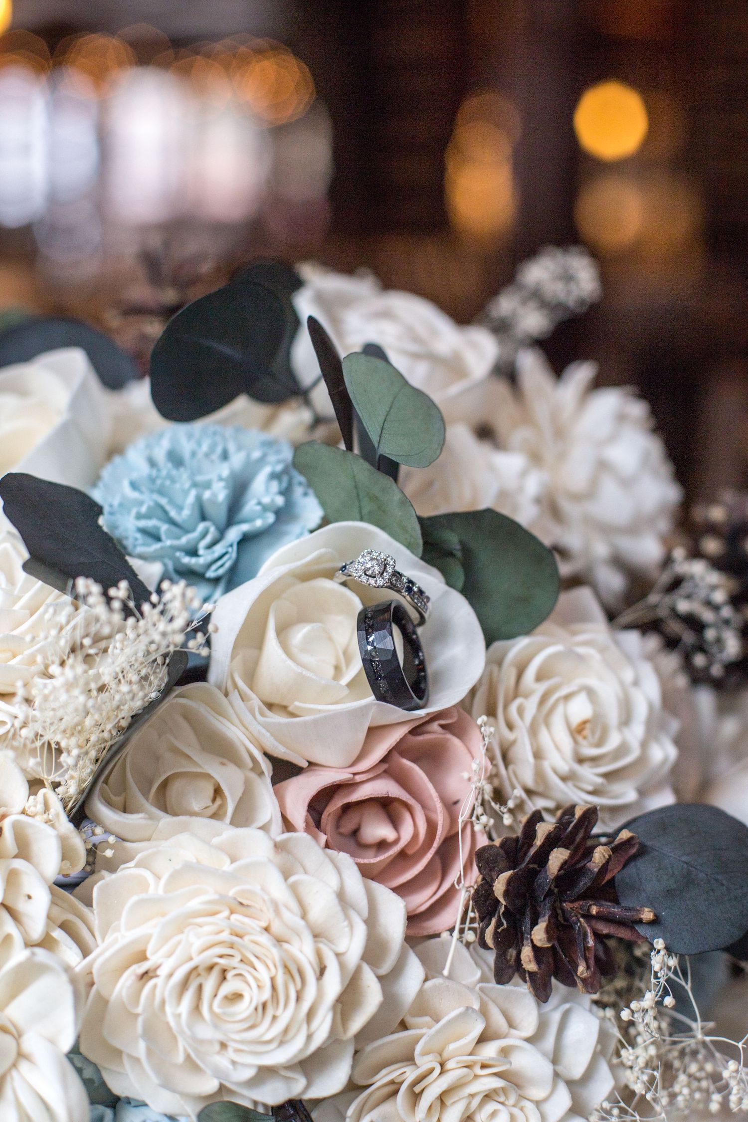 Elegant wedding bouquet with white, pink, and blue flowers featuring wedding rings nestled among roses and eucalyptus leaves.