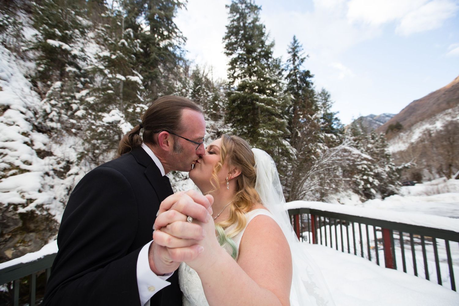 A couple shares a tender moment during their winter wedding with snow-covered evergreens in the background.