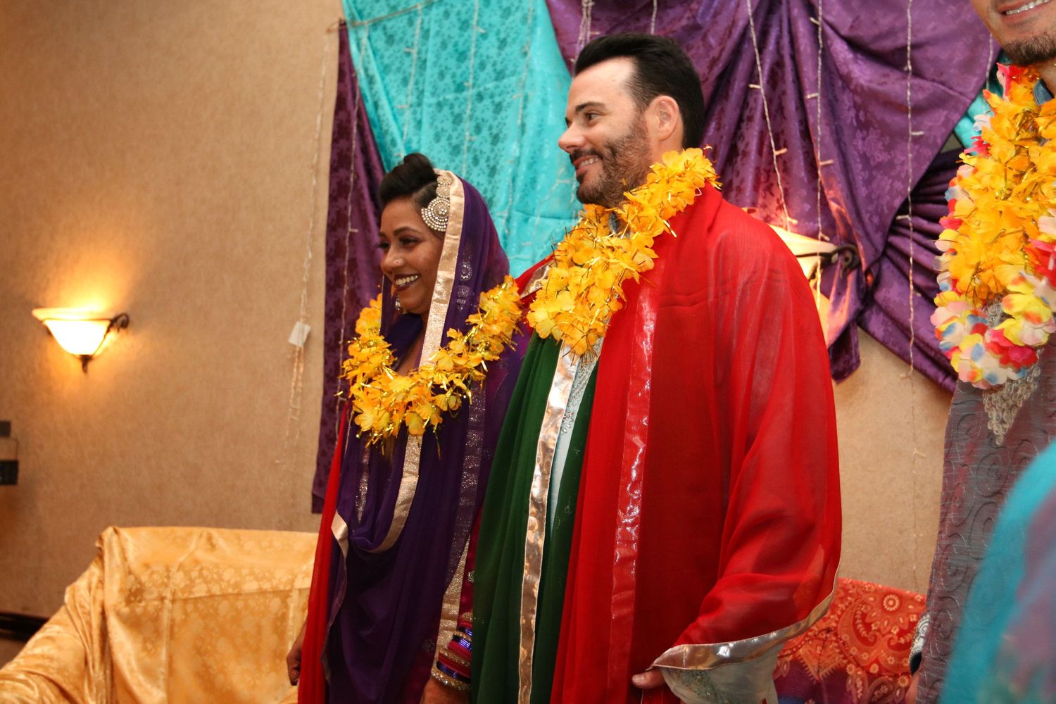 Two people wearing bright garlands and traditional Indian attire at a cultural celebration.