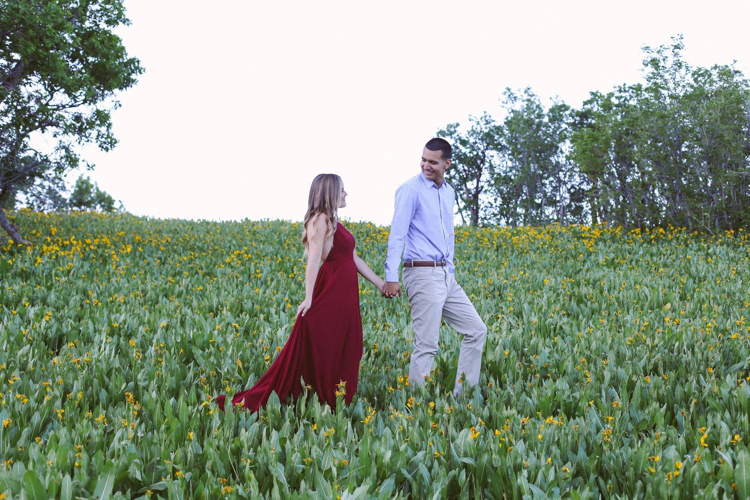 Couple walking through field of sunflowers, woman in flowing red dress.