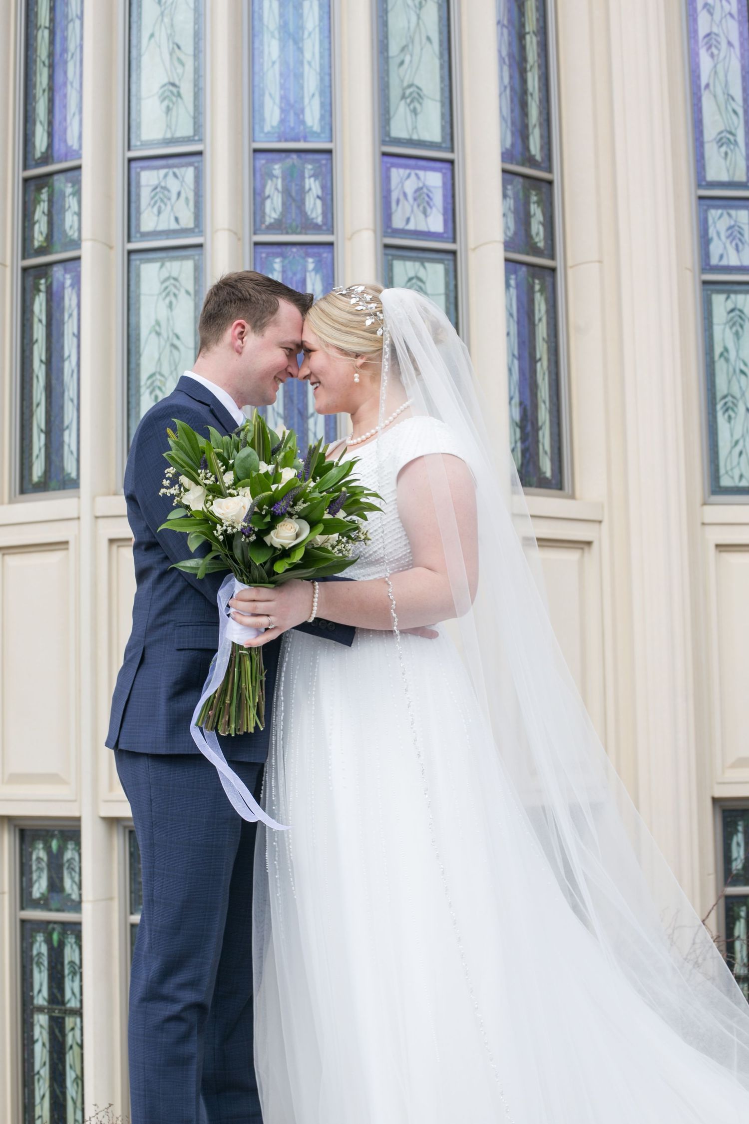 Couple shares tender moment in front of ornate stained glass windows.
