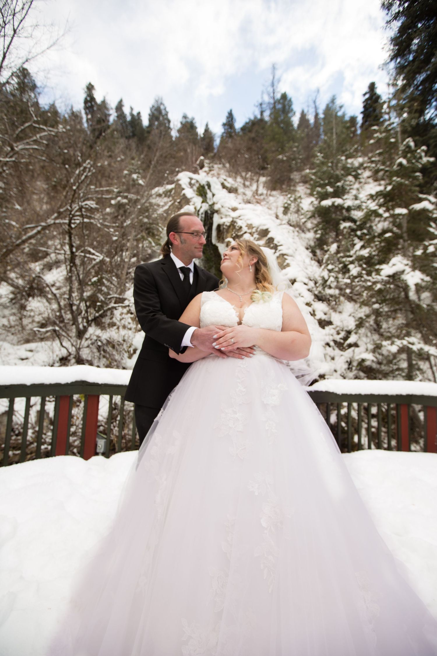 A couple in wedding attire shares a romantic moment on a snow-covered deck in winter.