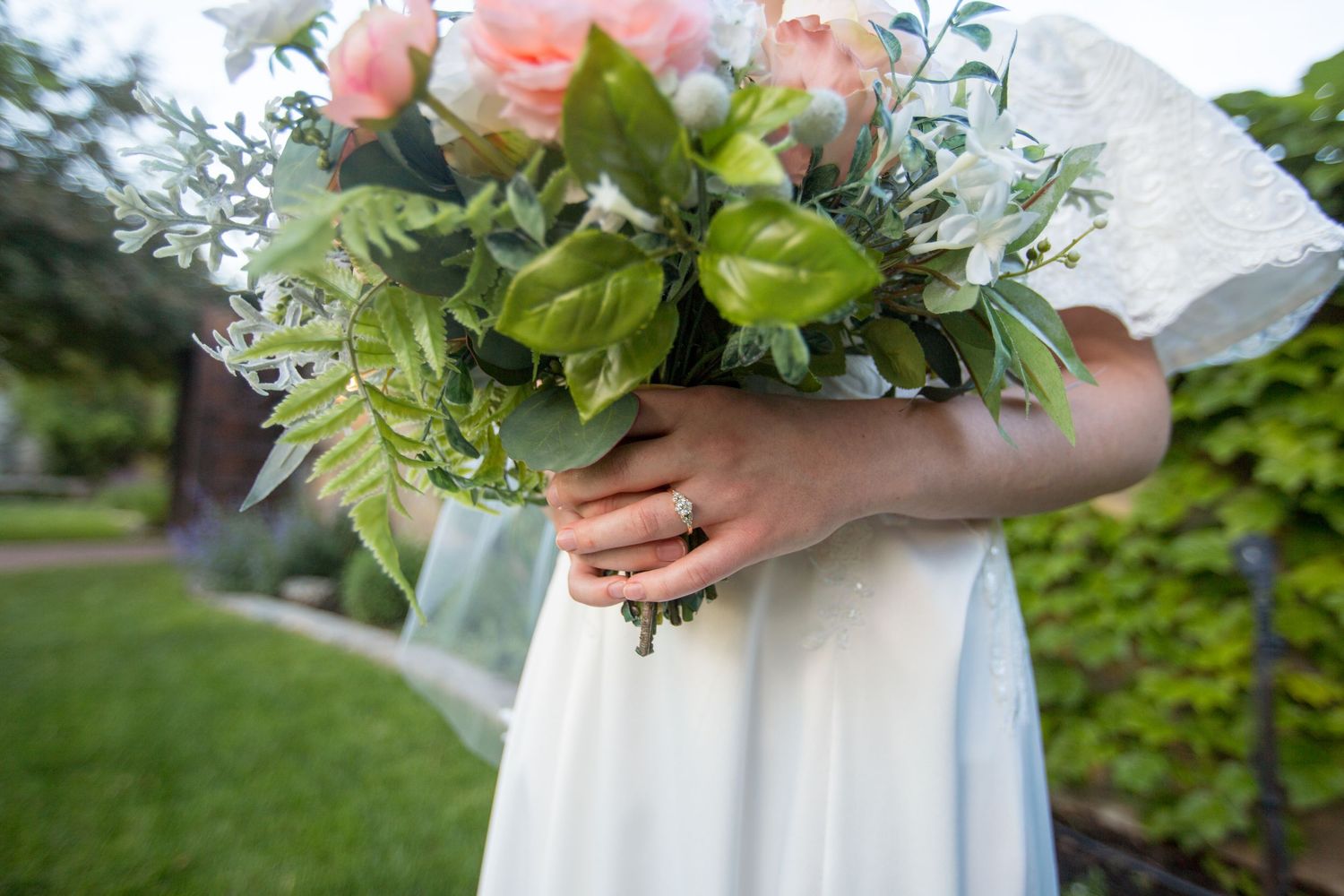 Detail shot of a pastel bridal bouquet with roses and greenery against a white dress.