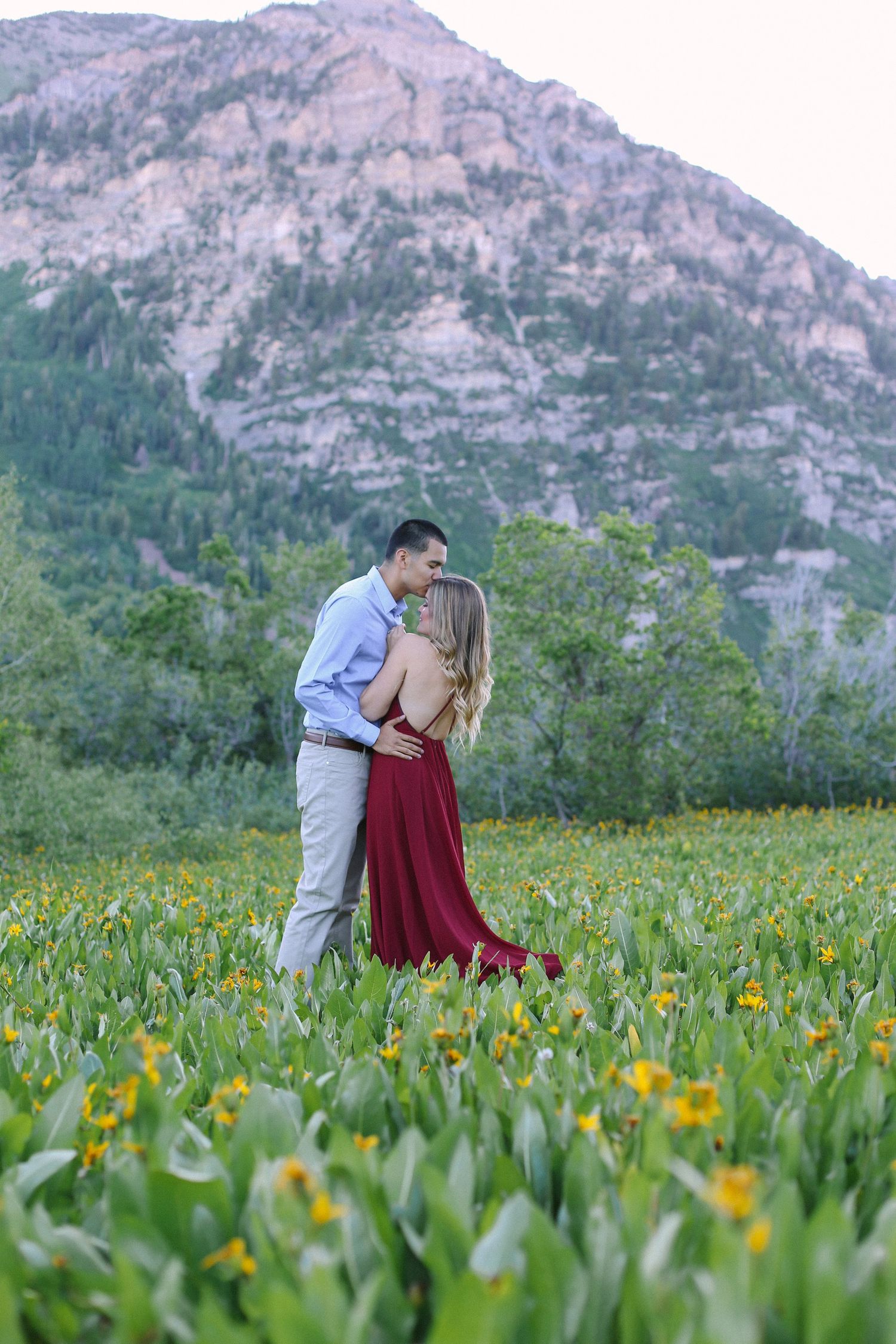 Romantic couple embracing in a meadow of wildflowers with mountain backdrop.
